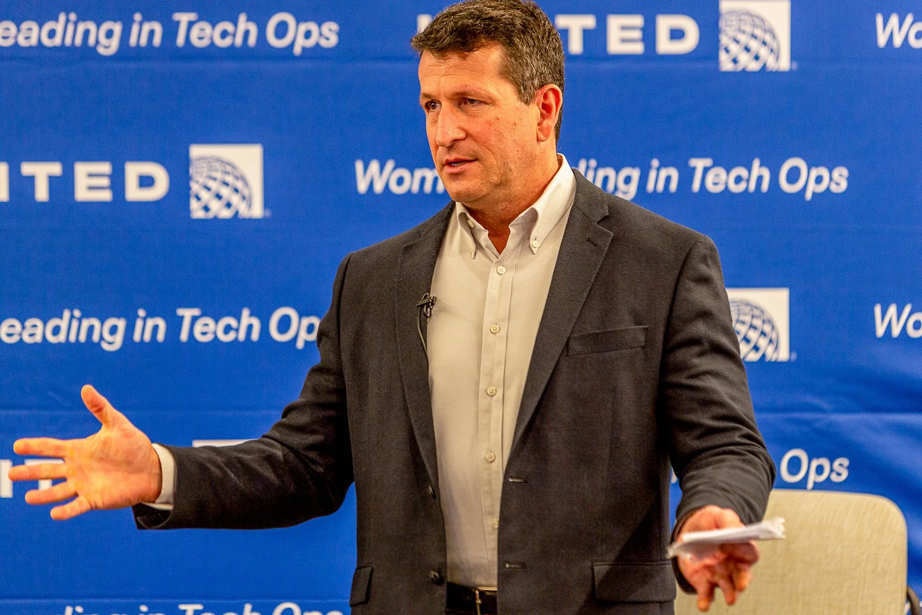 Man in a suit giving a presentation at an event with a blue backdrop that reads "Leading in Tech Ops" and "WOMEN in Tech Ops".©2026 Steven Barston