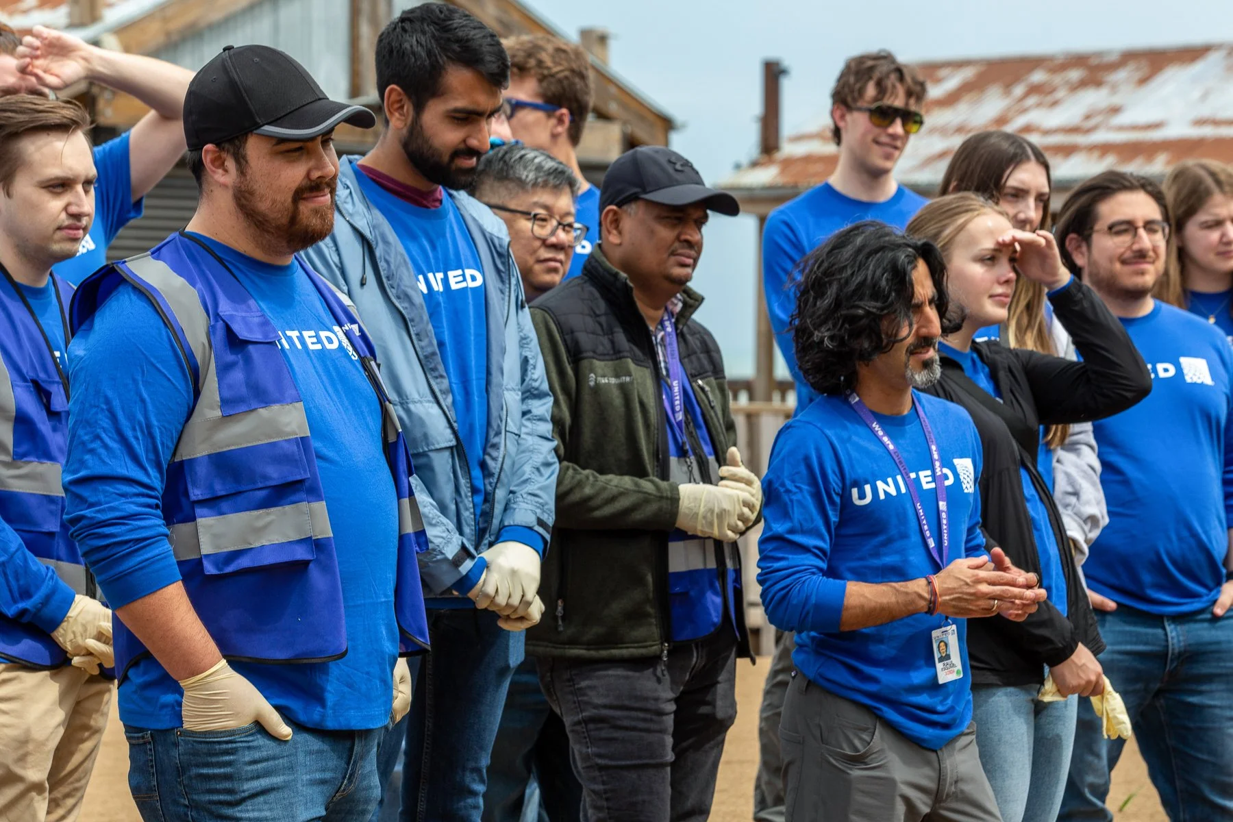 Group of people standing outdoors, wearing blue shirts and safety vests, participating in a community service or volunteer event.