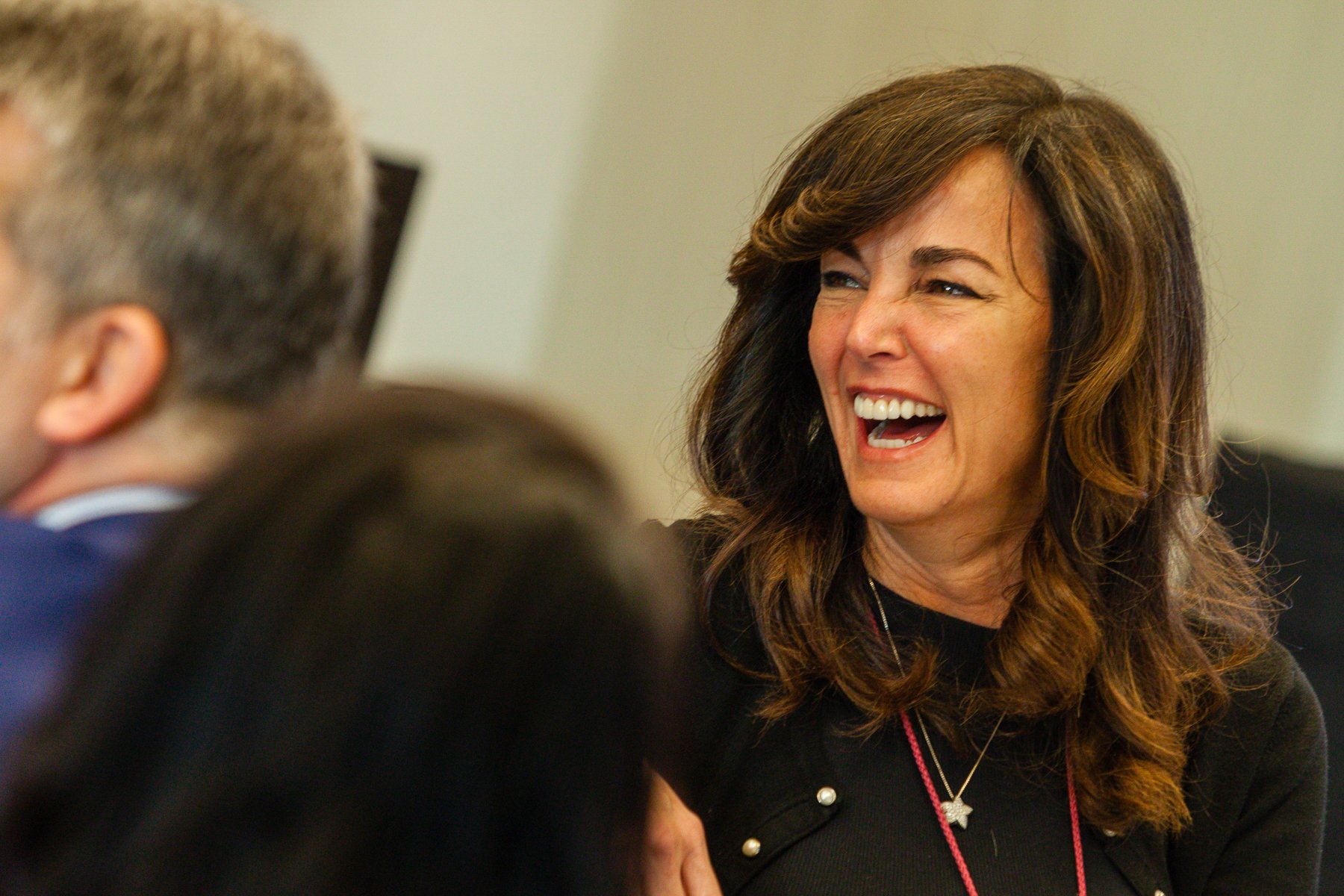 Woman with brown hair laughing while talking to a man in a professional setting.