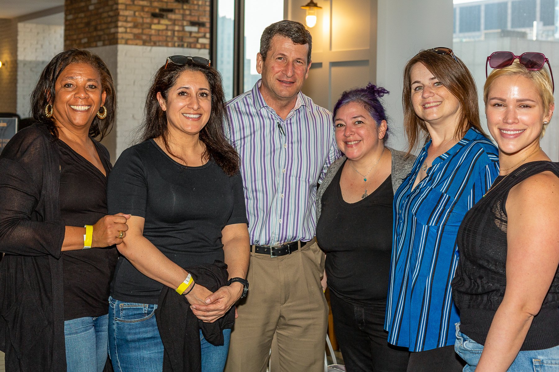 Group of seven diverse people standing together indoors, smiling, at a social event or gathering.