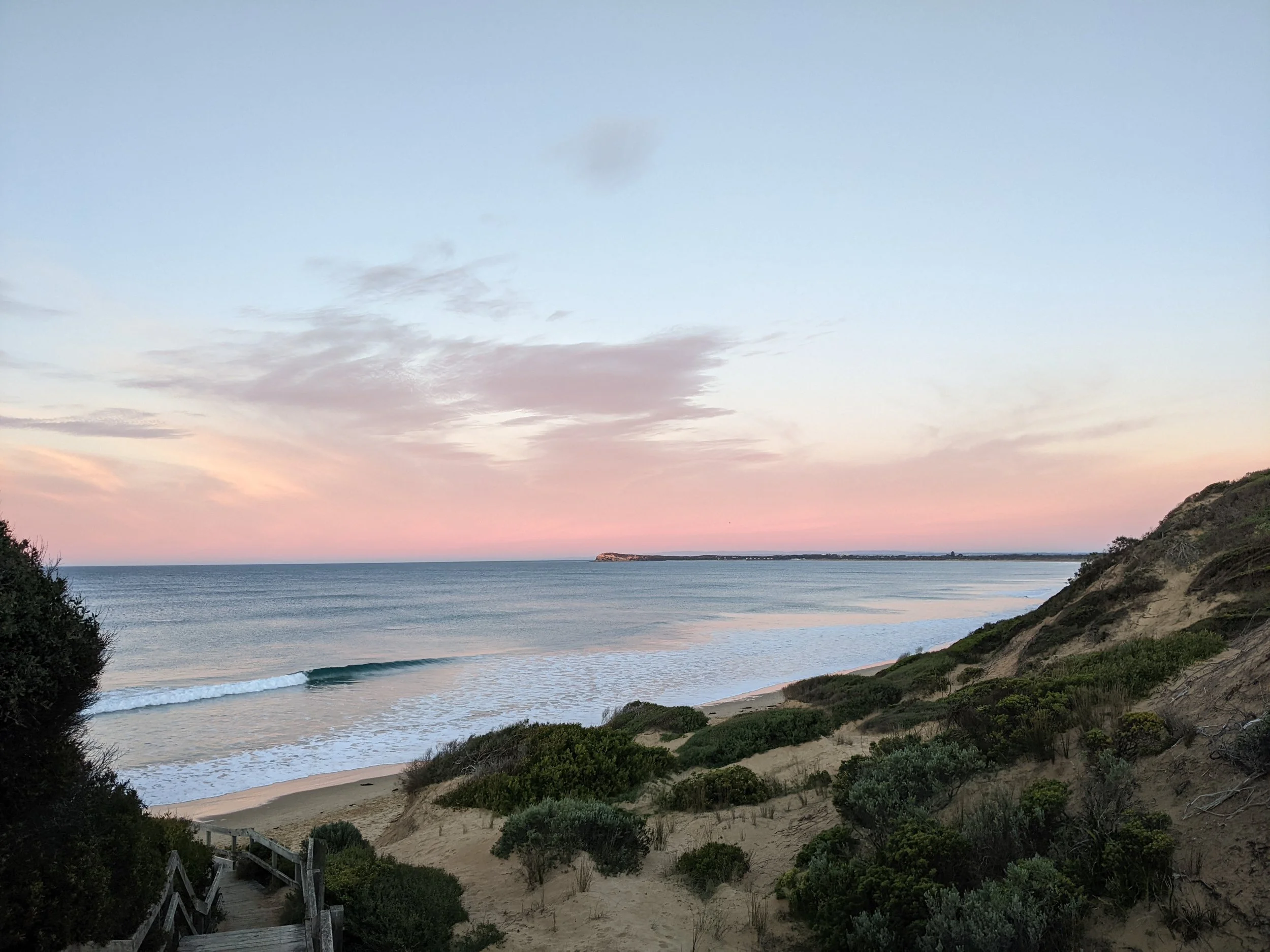 Ocean Grove beach at sunset with waves, sandy shore, green bushes, the bluff in the background.