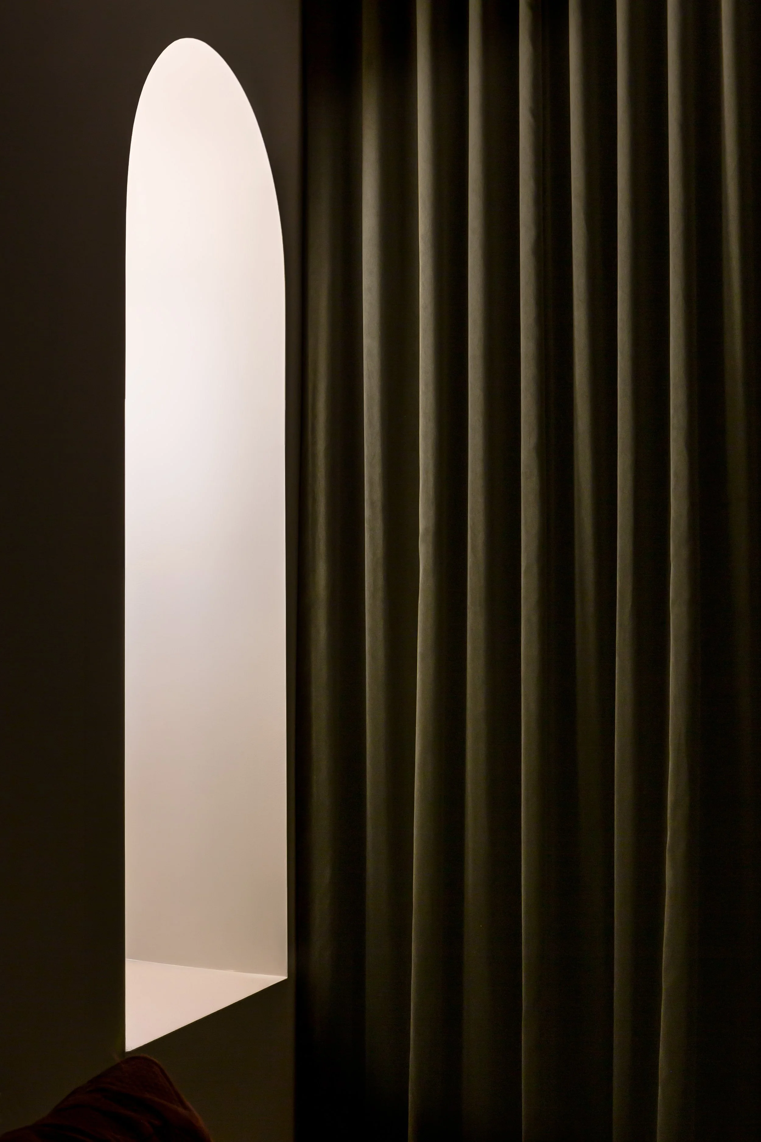 Close-up of partially open vertical blinds with a white cut-out shape of a rectangle with a semi-circular top on a wall behind the blinds.
