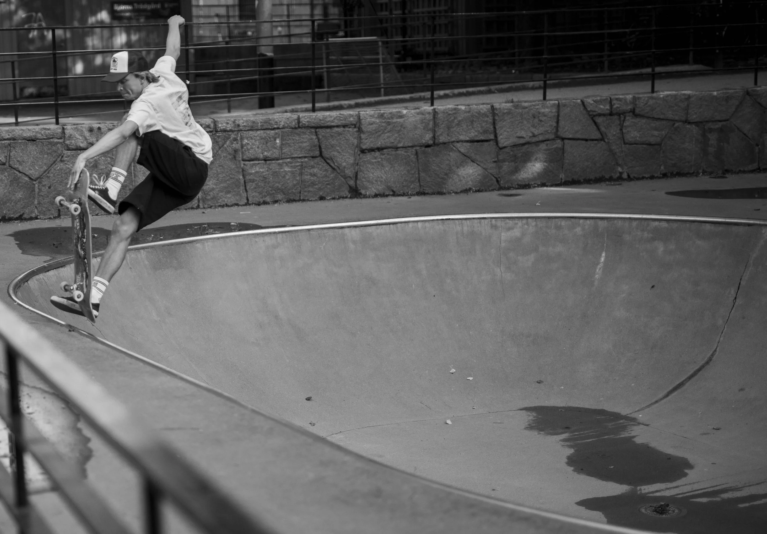 A person skateboarding in a skate park, captured in black and white, showing a mid-air trick over the edge of a skate bowl.