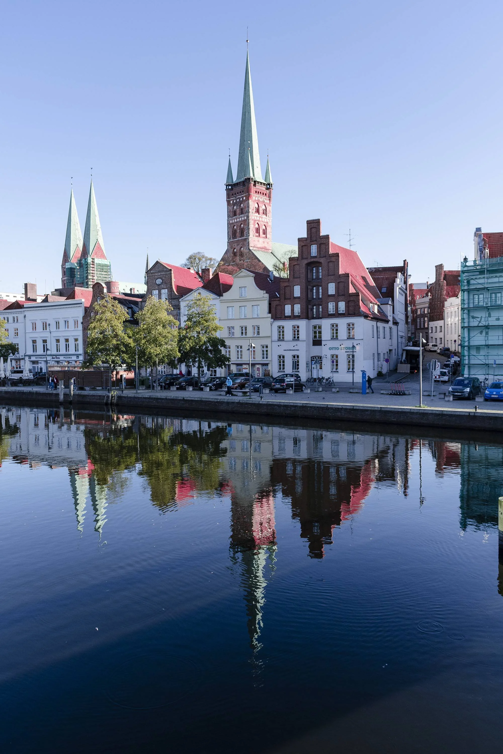 View of a cityscape with historic buildings and church spires reflected in the river below, with clear blue sky.