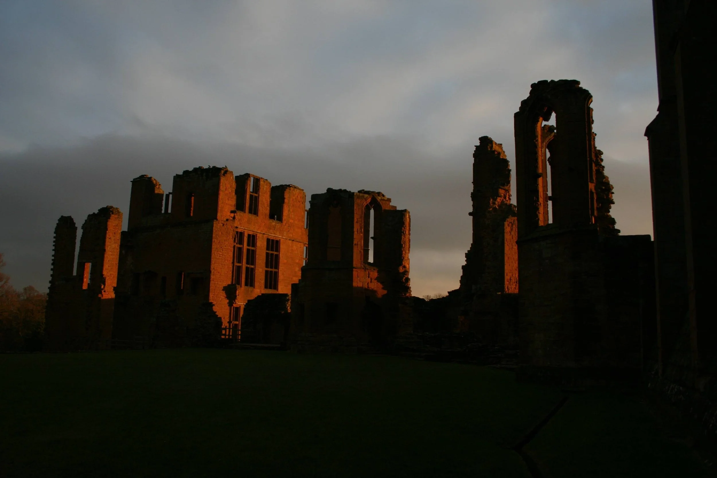 Ruins of a historic stone building at sunset with a cloudy sky in the background.