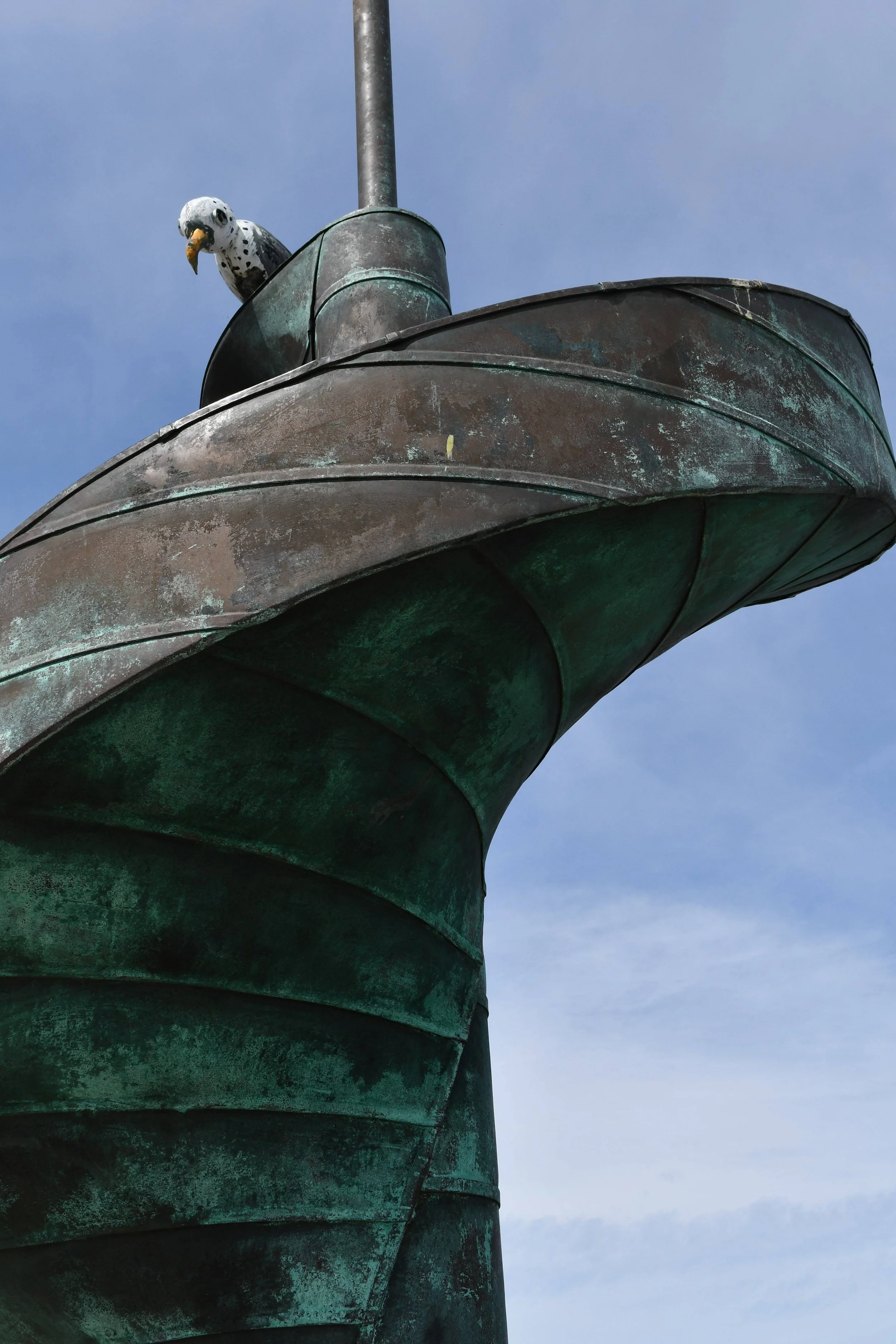 Close-up of a statue with a fake seagull perched on it, against a blue sky background.