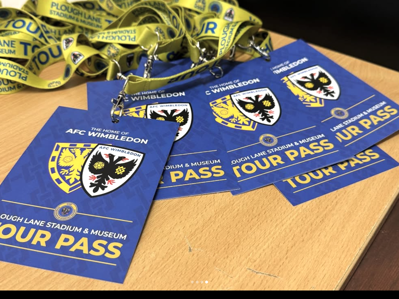 Multiple blue tickets and yellow lanyards with the AFC Wimbledon logo, promoting the stadium tours  and museum, on a wooden table.