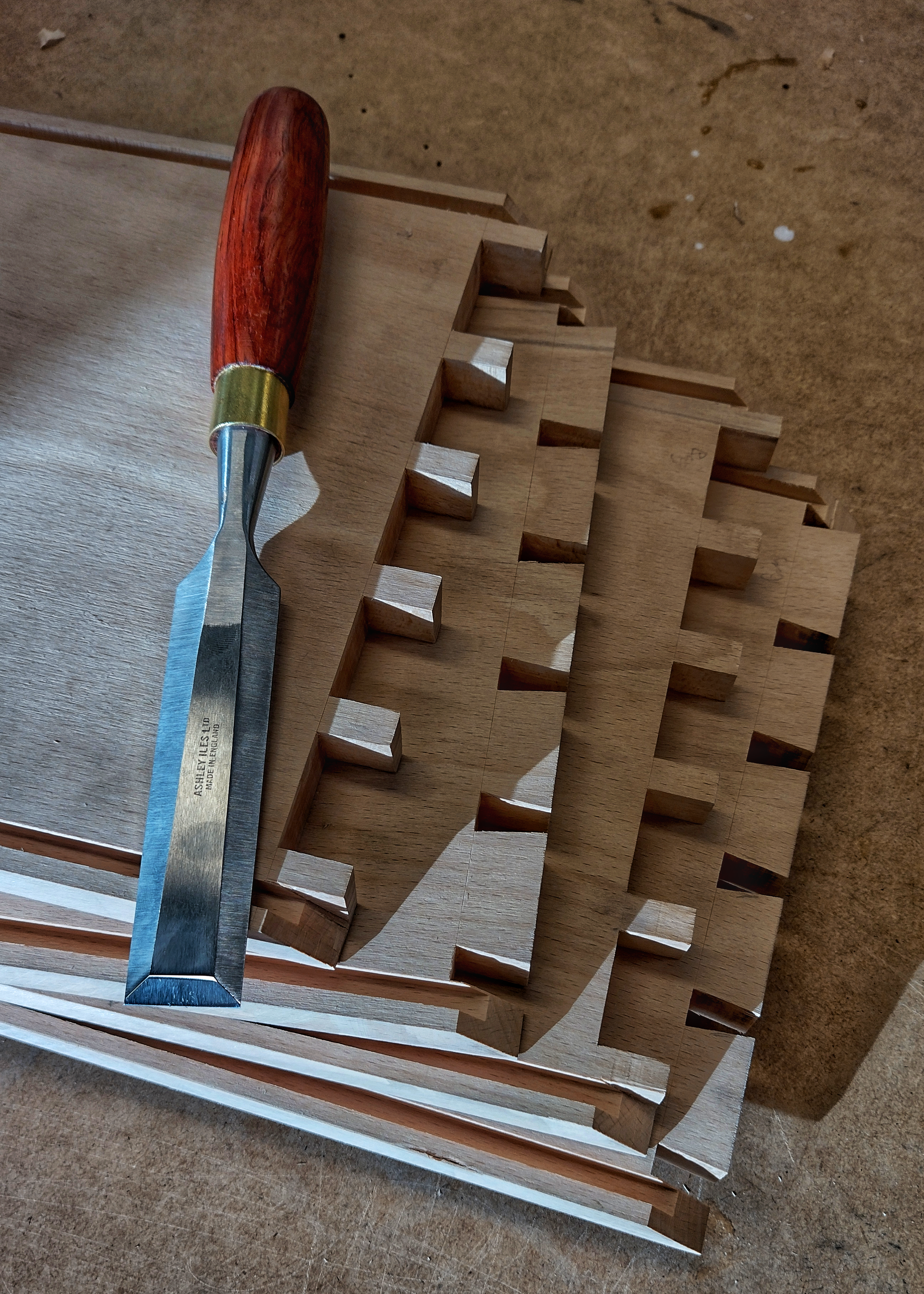 Close-up of a woodworking step stool with a handle, showing cutouts on each step, made of unfinished light wood, placed on a wooden work surface.