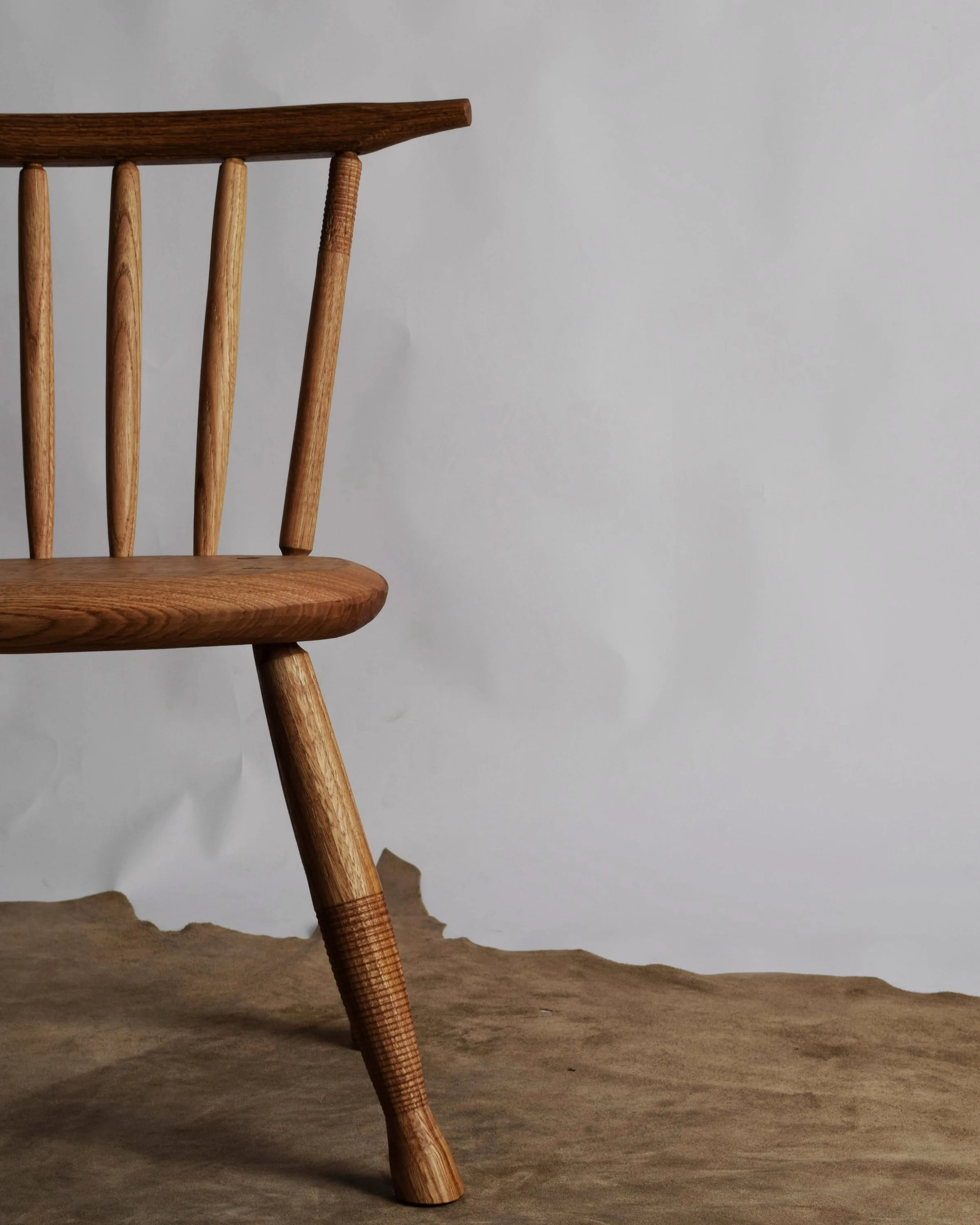 Close-up of a wooden chair with vertical spindles and angled legs on a textured brown surface against a plain light gray background.