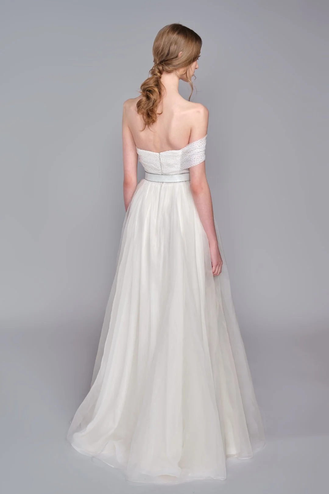 Woman in a white off-the-shoulder dress, viewed from the back, with a gray background.