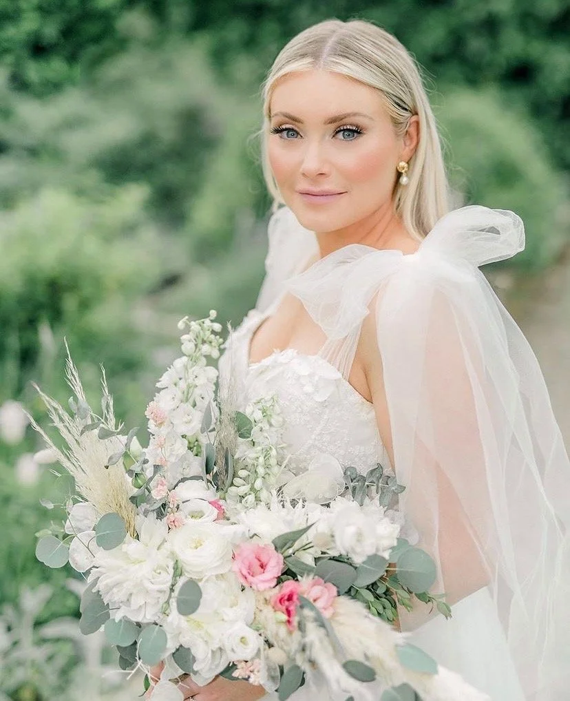 A bride in a white wedding dress holding a bouquet of white and pink flowers outdoors.