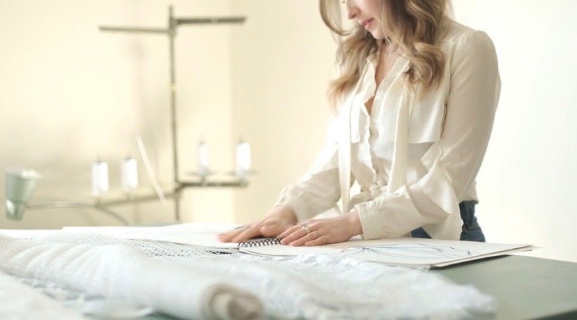 A woman in a white blouse looking at rolled-out fabric in a sewing or fashion design studio.
