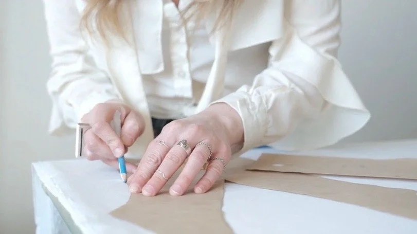 Person wearing a white blouse working on a fabric or paper with a pencil.