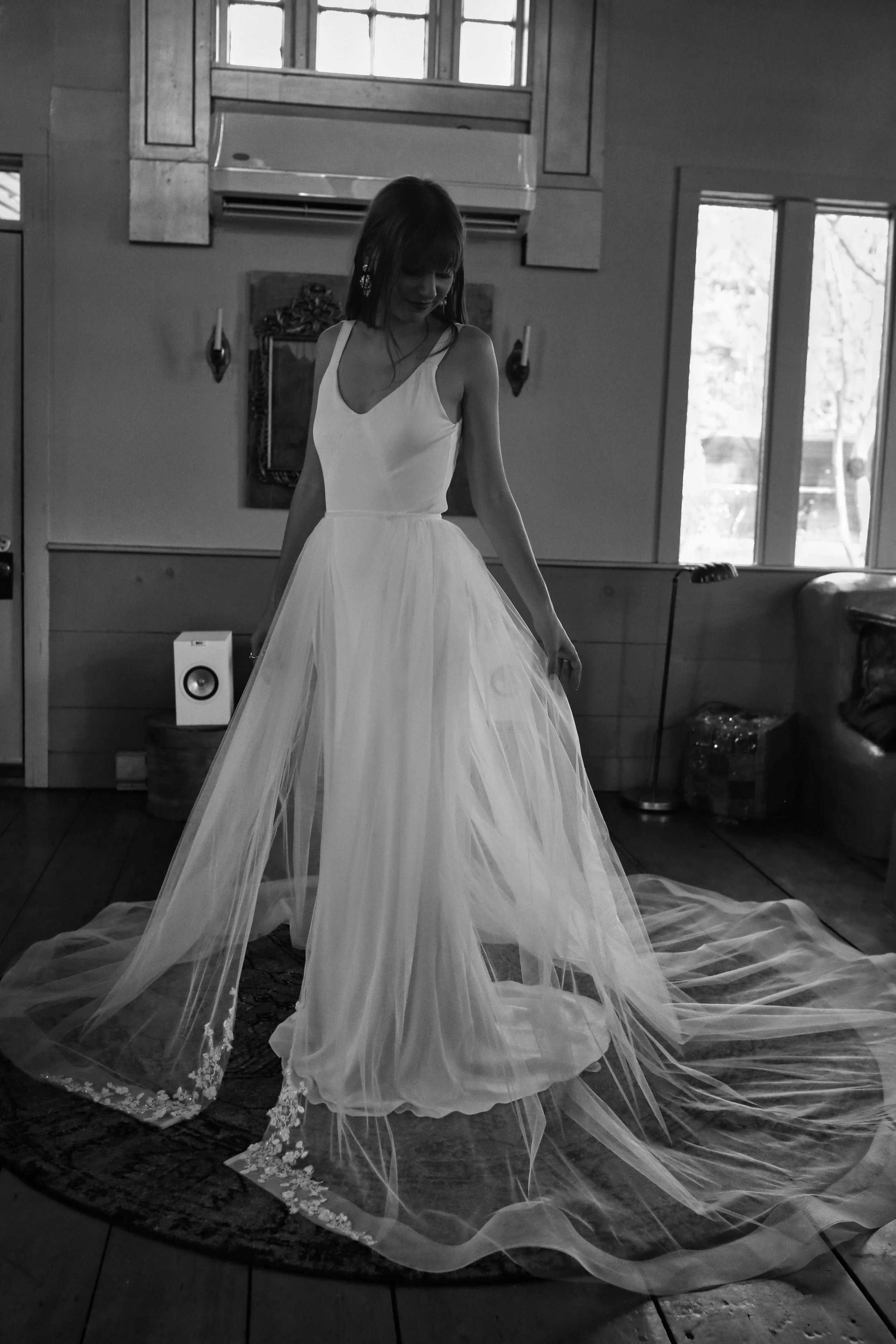 A woman in a wedding dress standing indoors in front of windows.