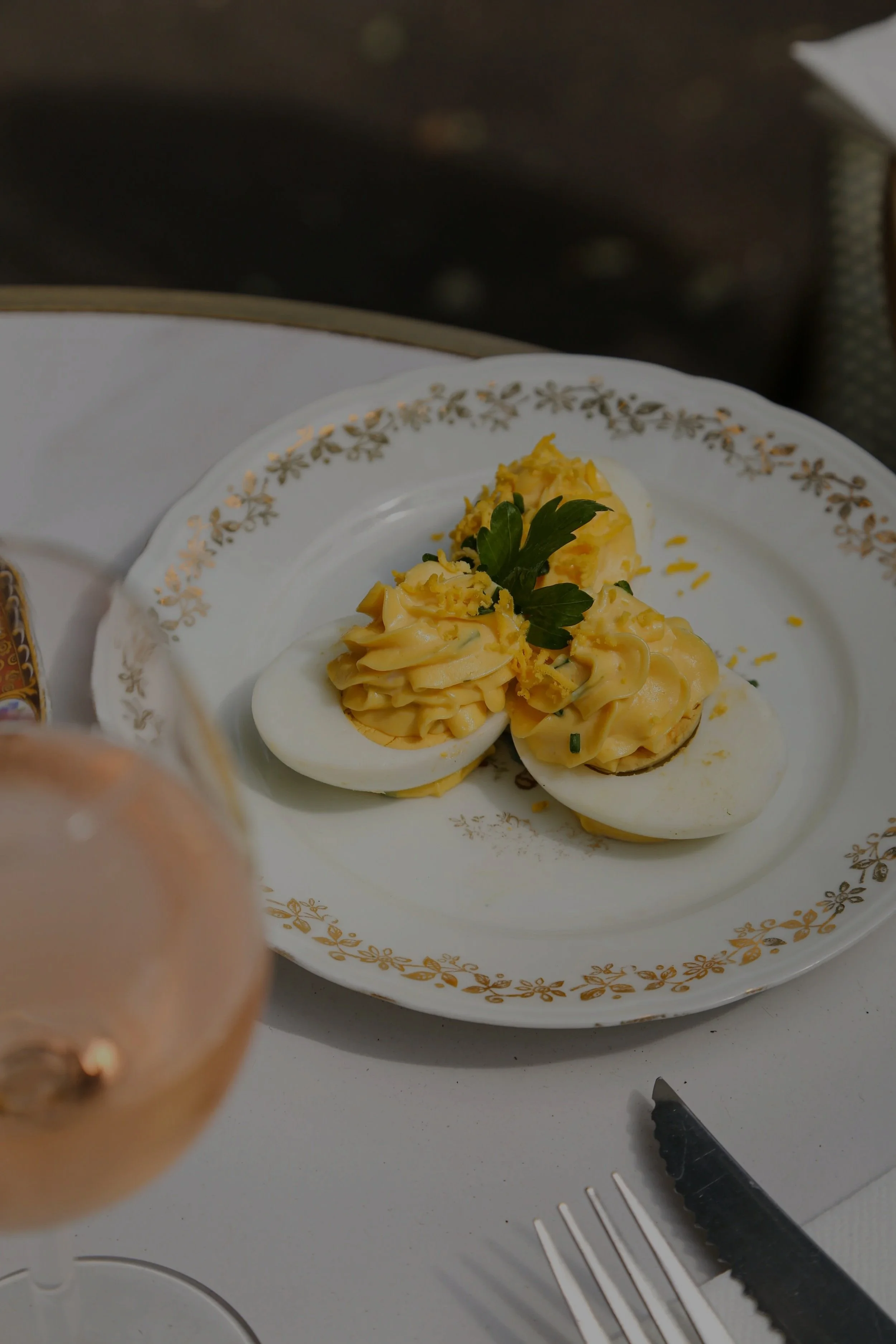 Oeufs durs coupés en deux garnis de fromage râpé et de persil, servis sur une assiette blanche avec motifs dorés.