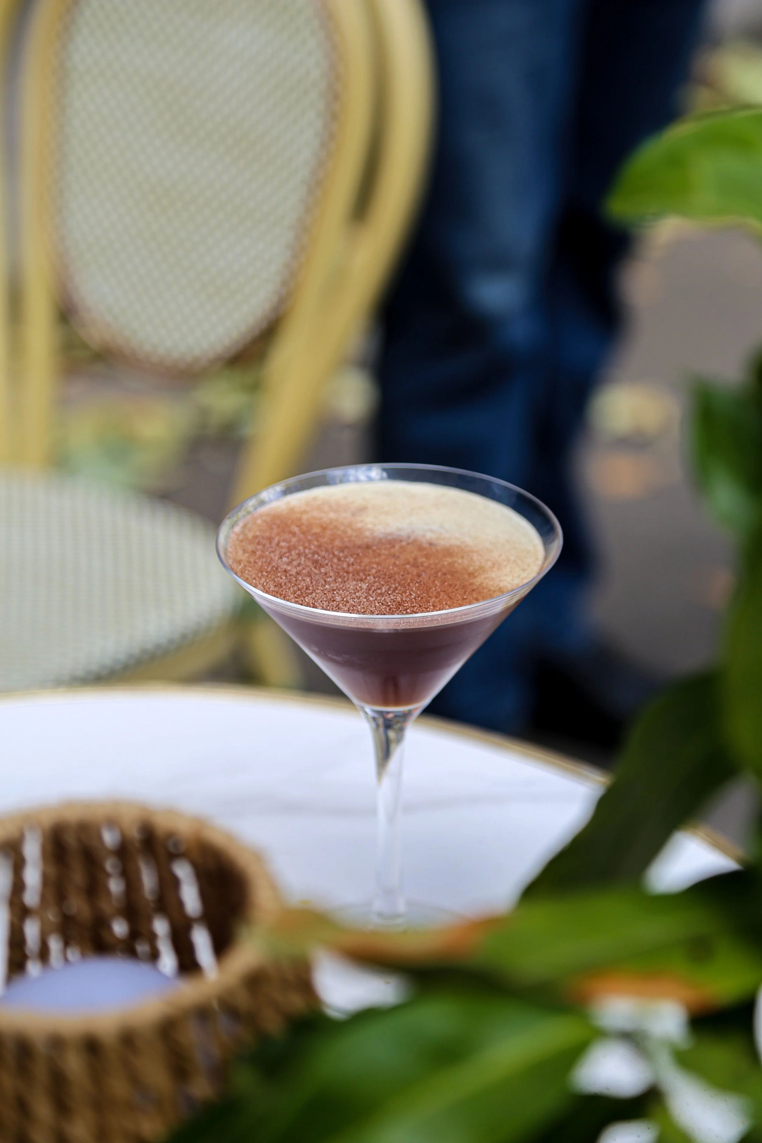 Verre à cocktail avec un dessert au cacao en poudre, entouré de chaises jaunes, d'une plante verte et d'éléments de décoration