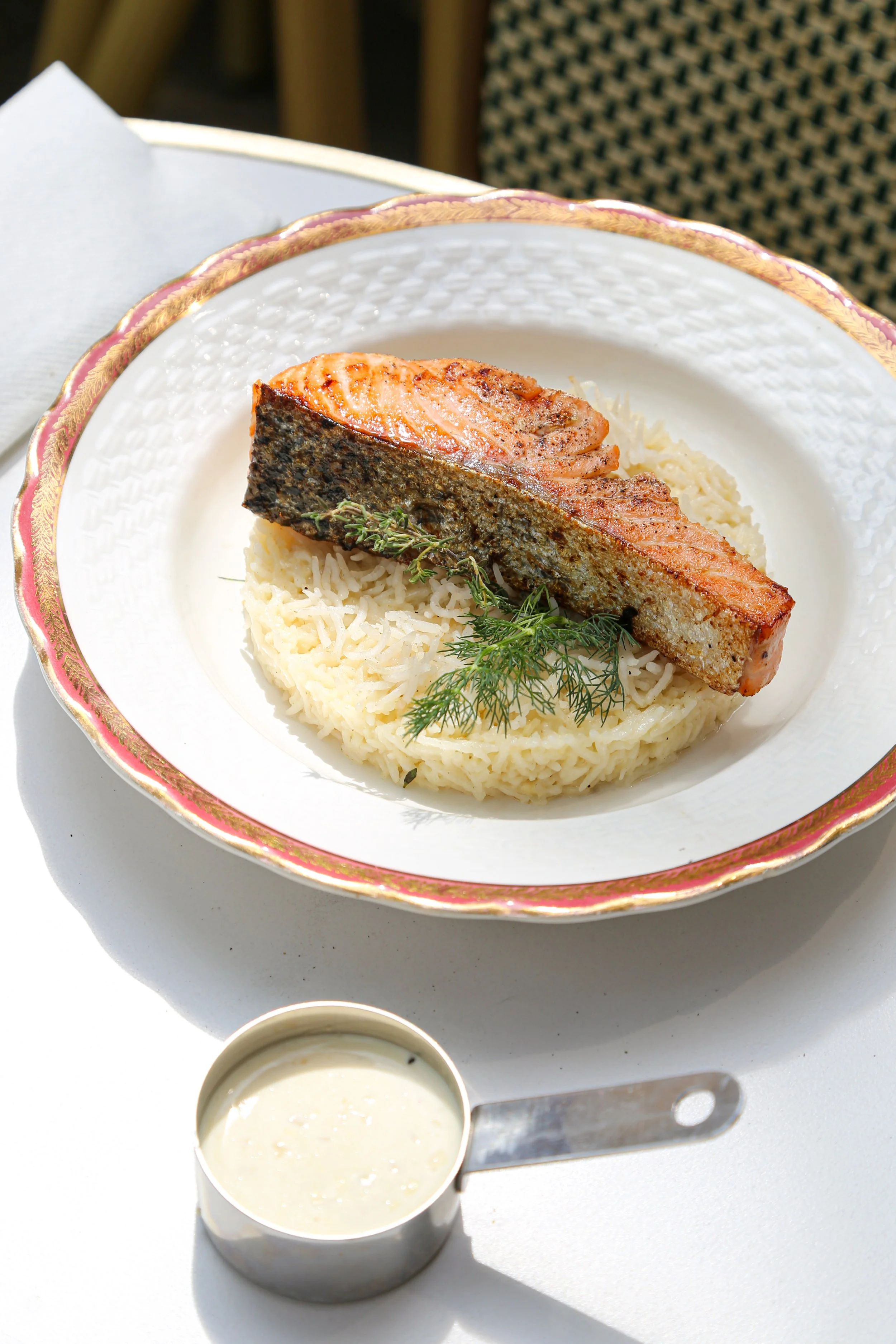 Assiette avec un filet de saumon grillé repose sur un lit de purée, garnie de brins de thym. Accompagnement dans un petit bol à sauce, avec un fond blanc extérieur, en extérieur avec lumière naturelle.