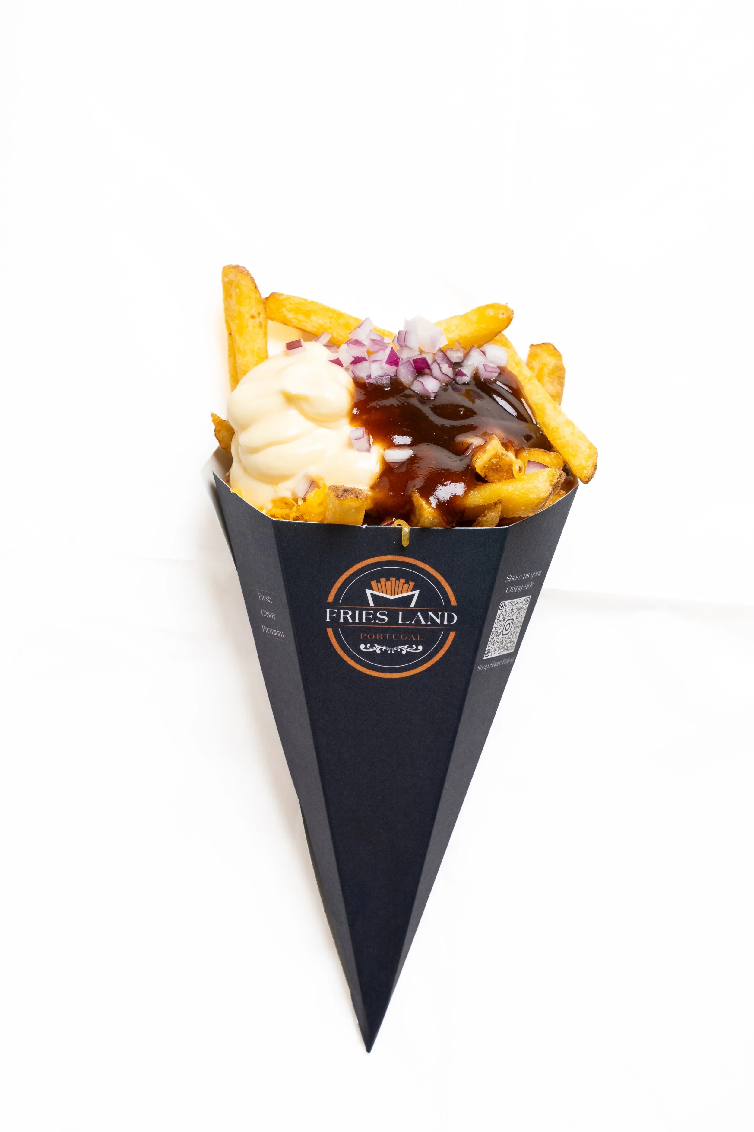 French fries with mayonnaise, topped with chopped red onions and barbecue sauce in a black paper cone from Frís Land Portugal.