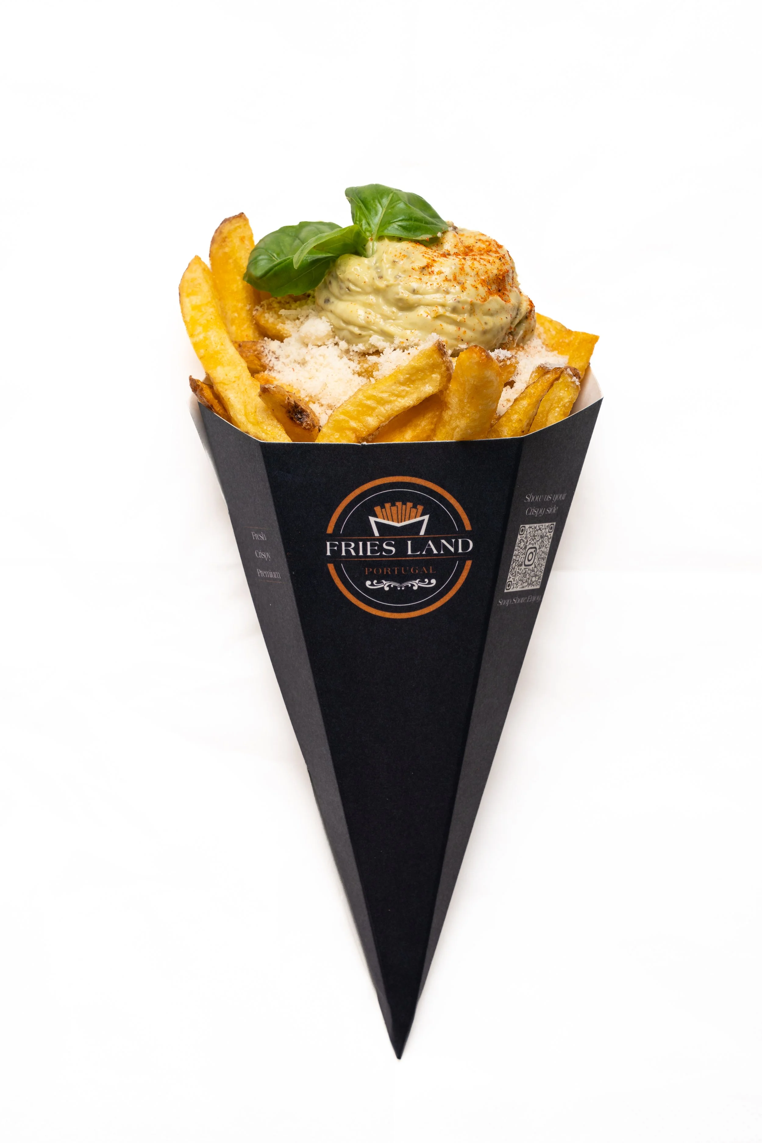 French fries topped with a creamy sauce, garnished with basil leaves, served in a black paper cone with a logo, set against a white background.
