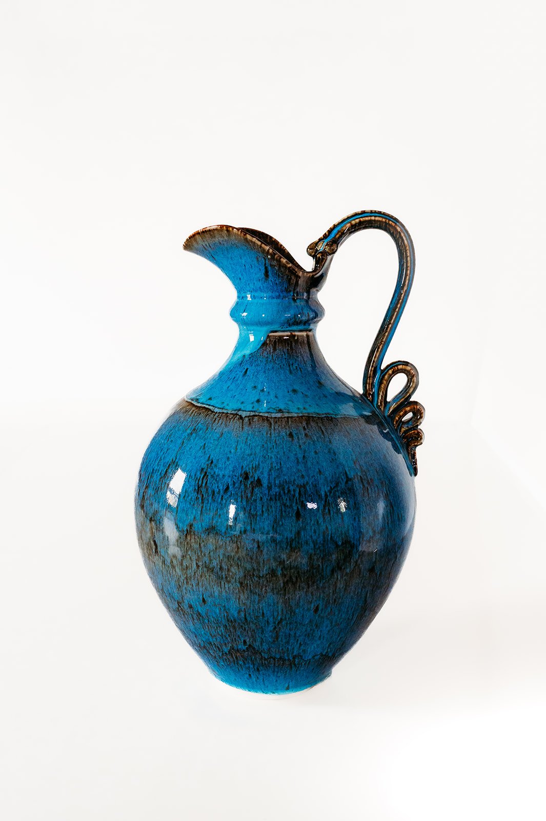 Blue ceramic pitcher with a decorative handle and a fish-shaped spout, set against a white background.