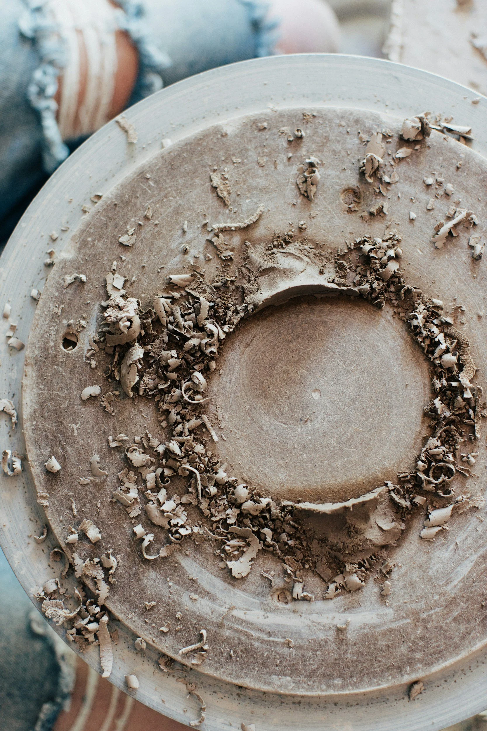 Close-up of a pottery wheel with wet clay, shavings, and curls of clay material on it, used for shaping ceramics.