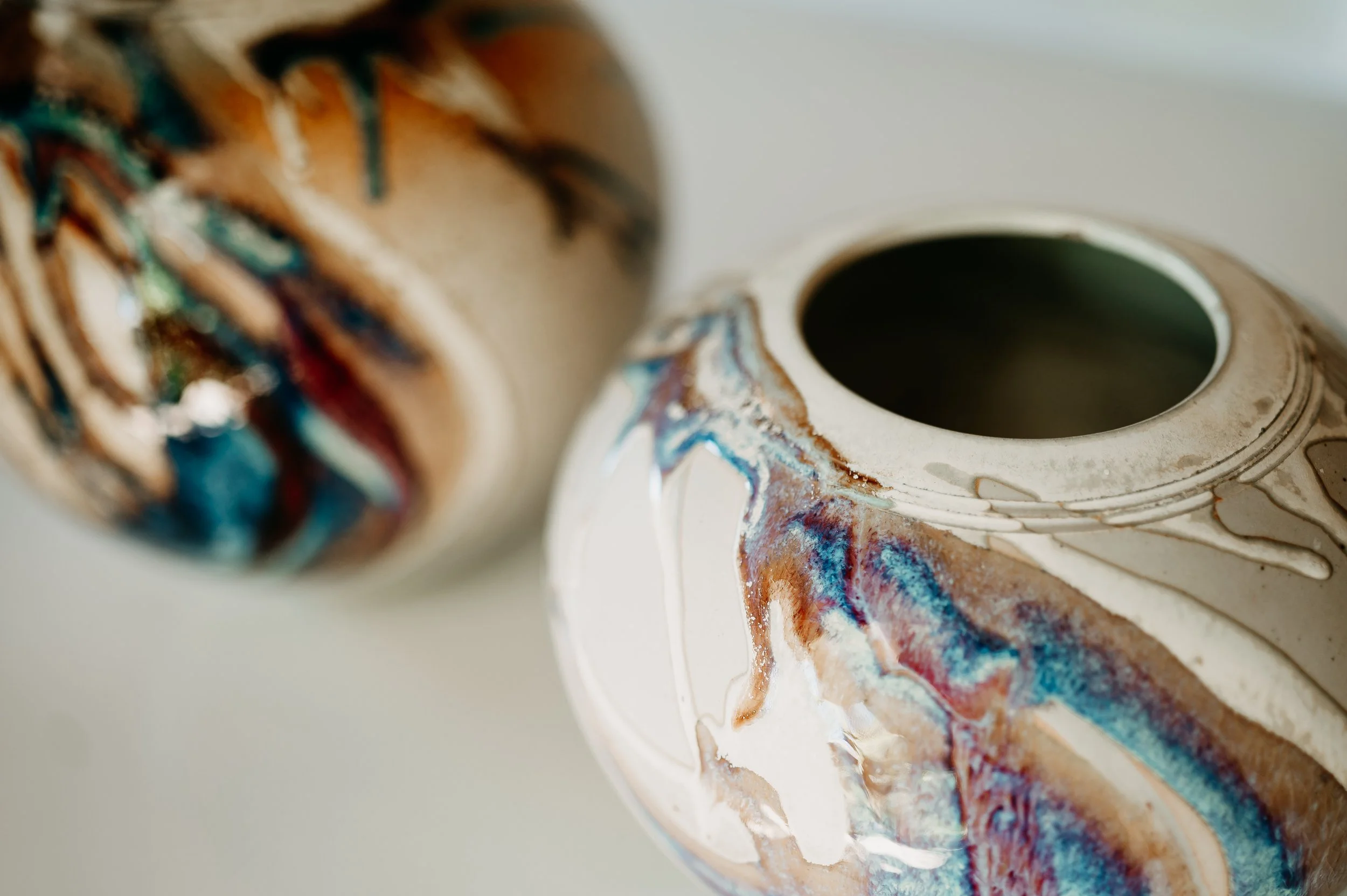 Close-up of a ceramic mug with a colorful, abstract glaze design and a dark interior.