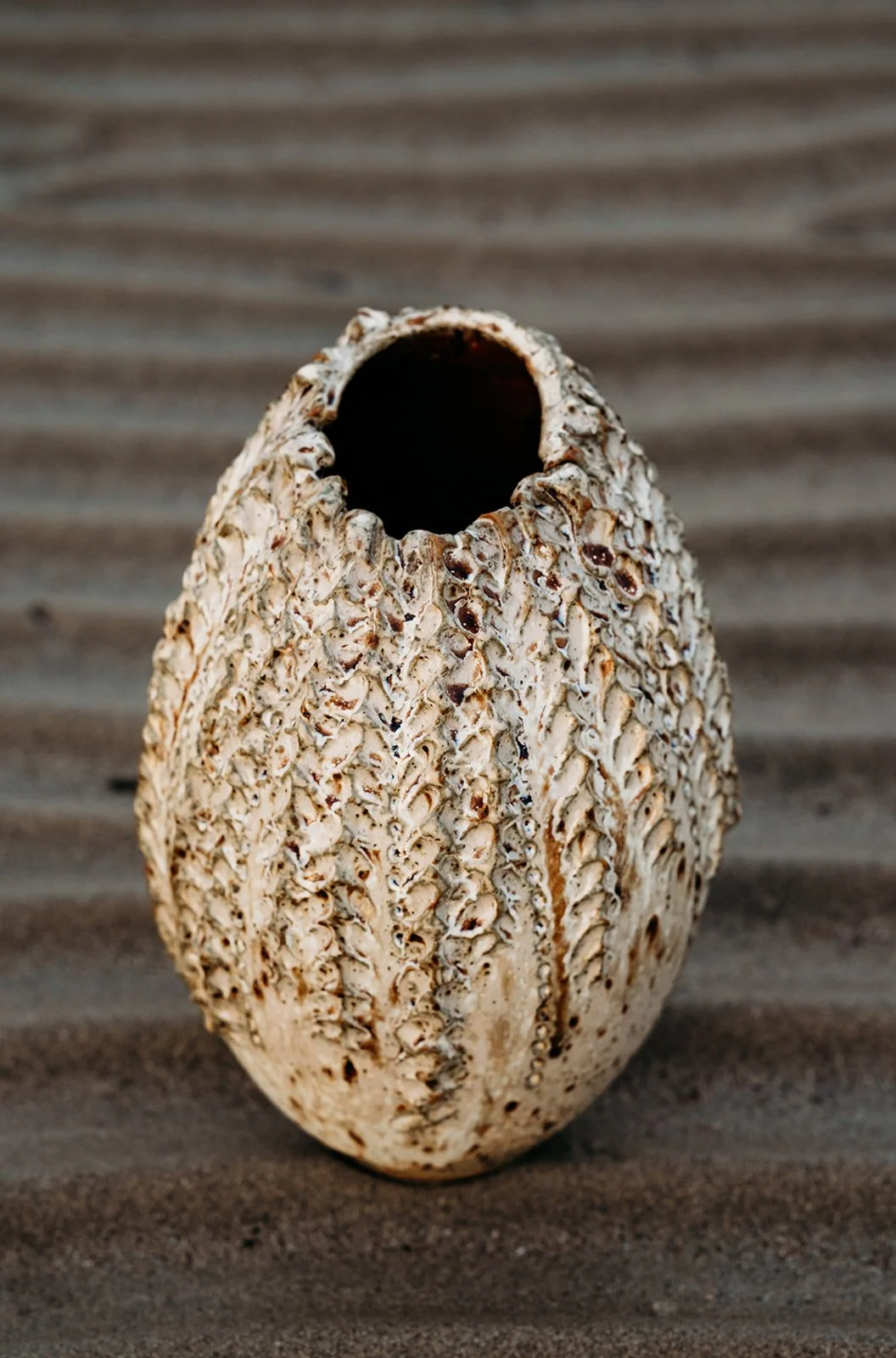 A decorative vase with a textured, shell-like surface, placed on a surface with a ridged pattern.
