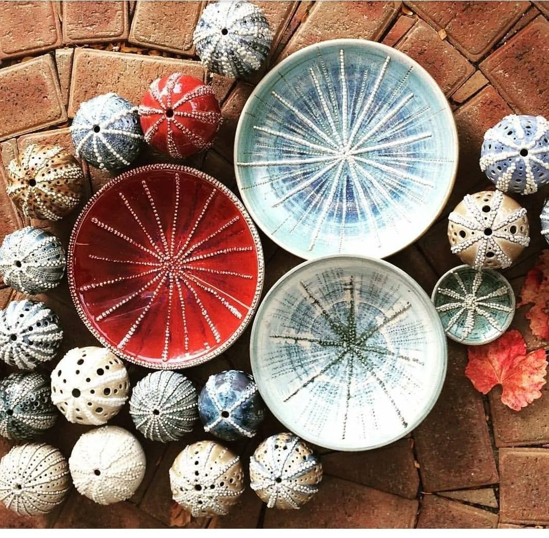 Decorative bowls and seashells arranged on a brick surface, with red, blue, and white shells surrounding small ceramic bowls with starfish patterns.