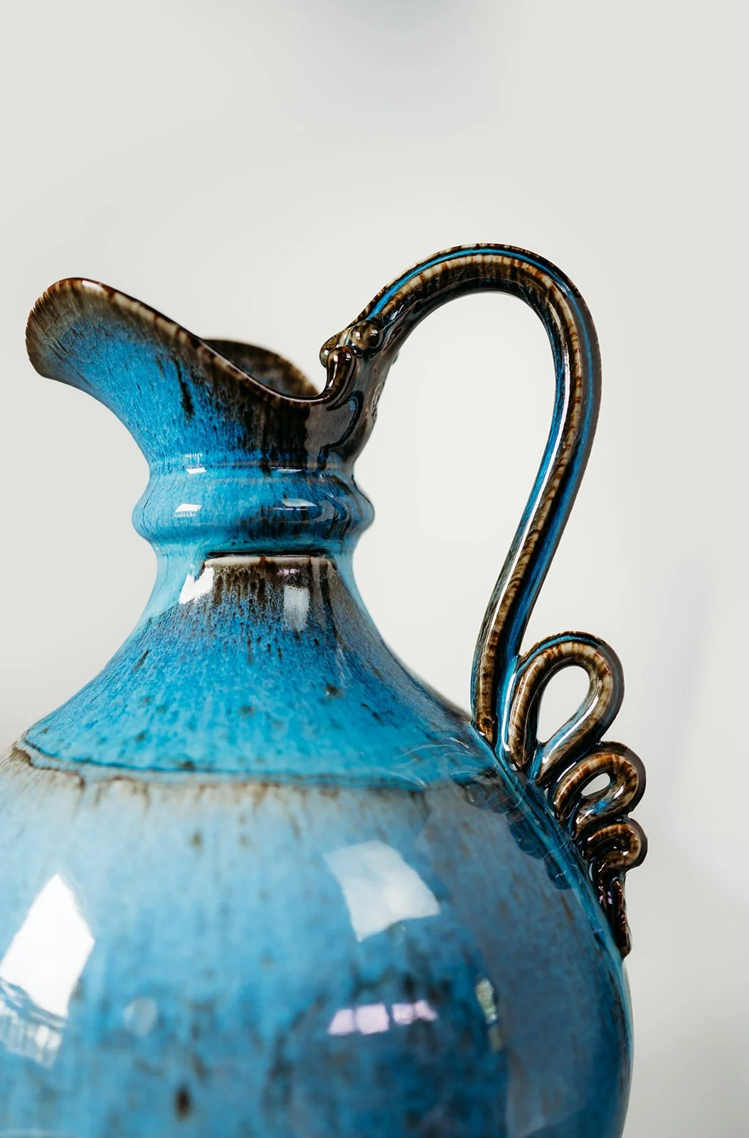 Close-up of a blue and brown ceramic vase with intricate handle design and a glossy surface.