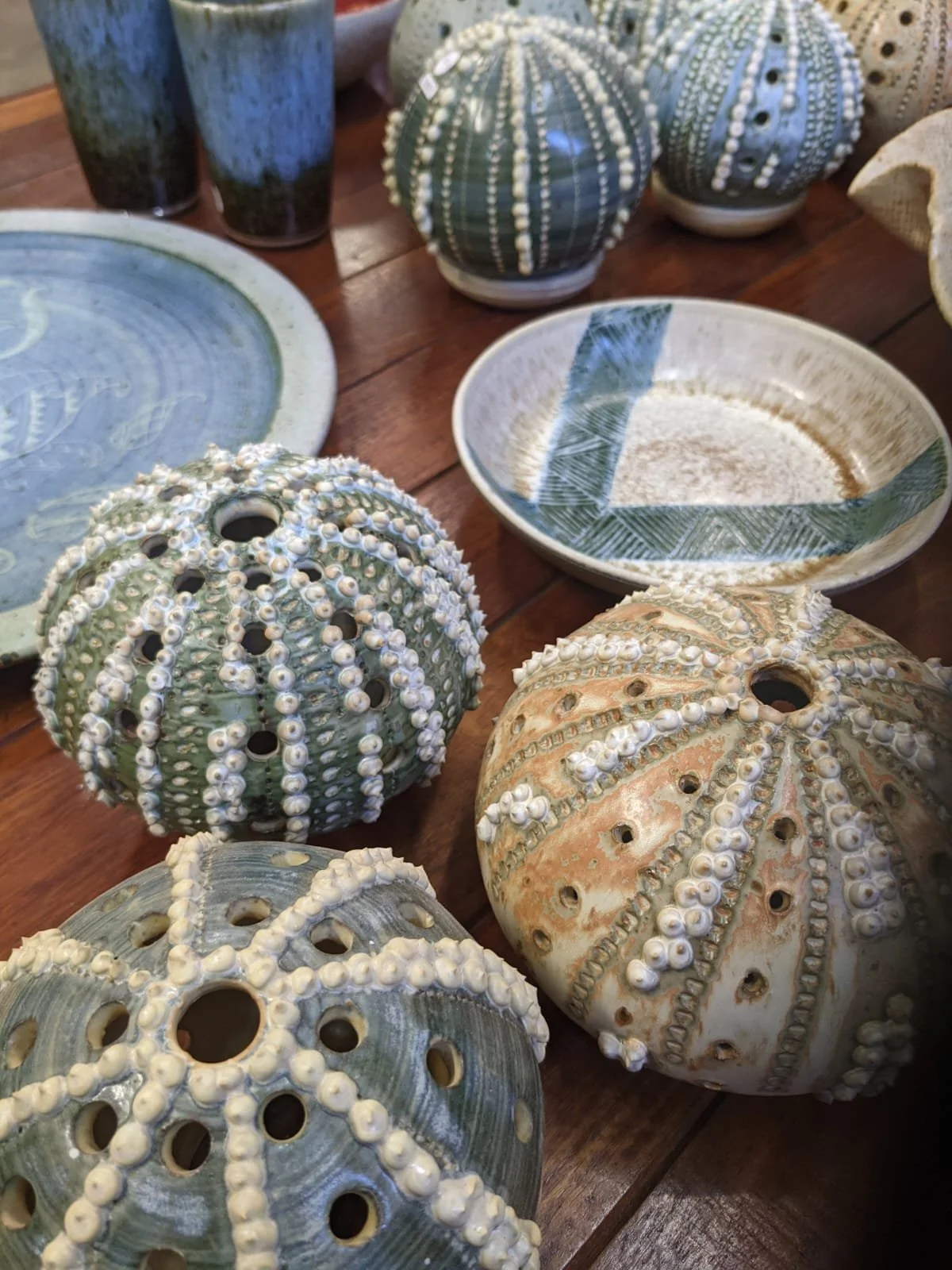 Various ceramic ornaments and bowls with sea urchin shell designs on a wooden table.