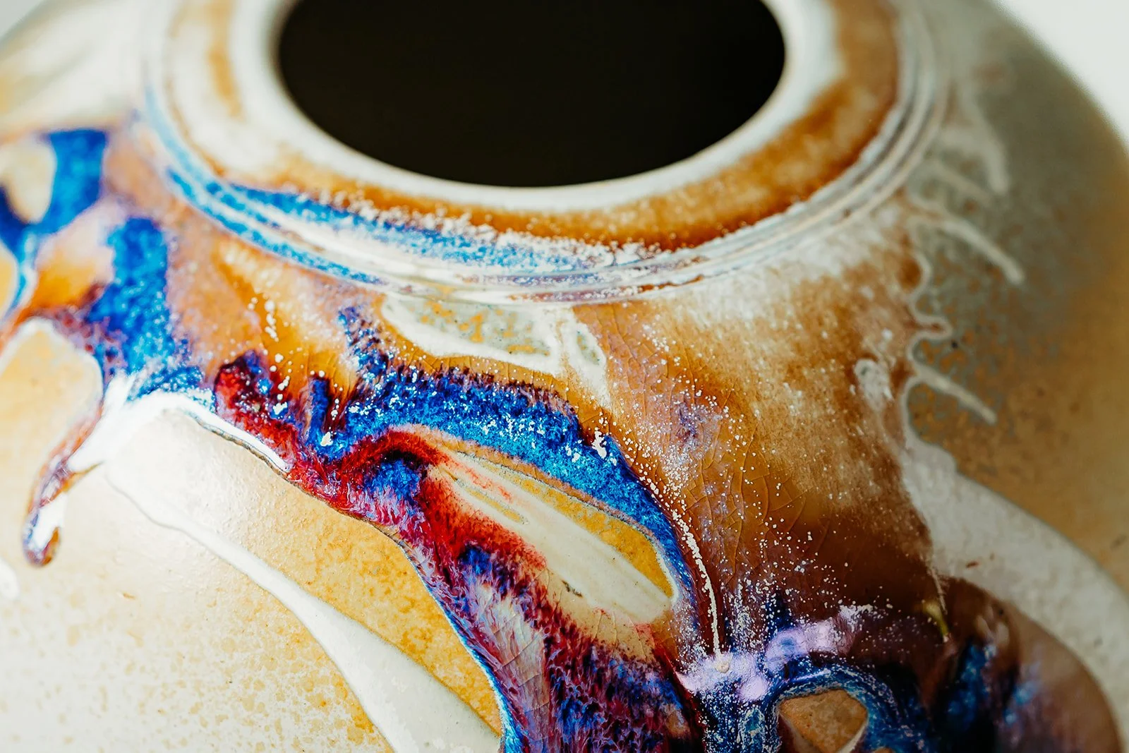 Close-up of a ceramic vase with abstract colorful glaze in blue, red, white, and tan hues.