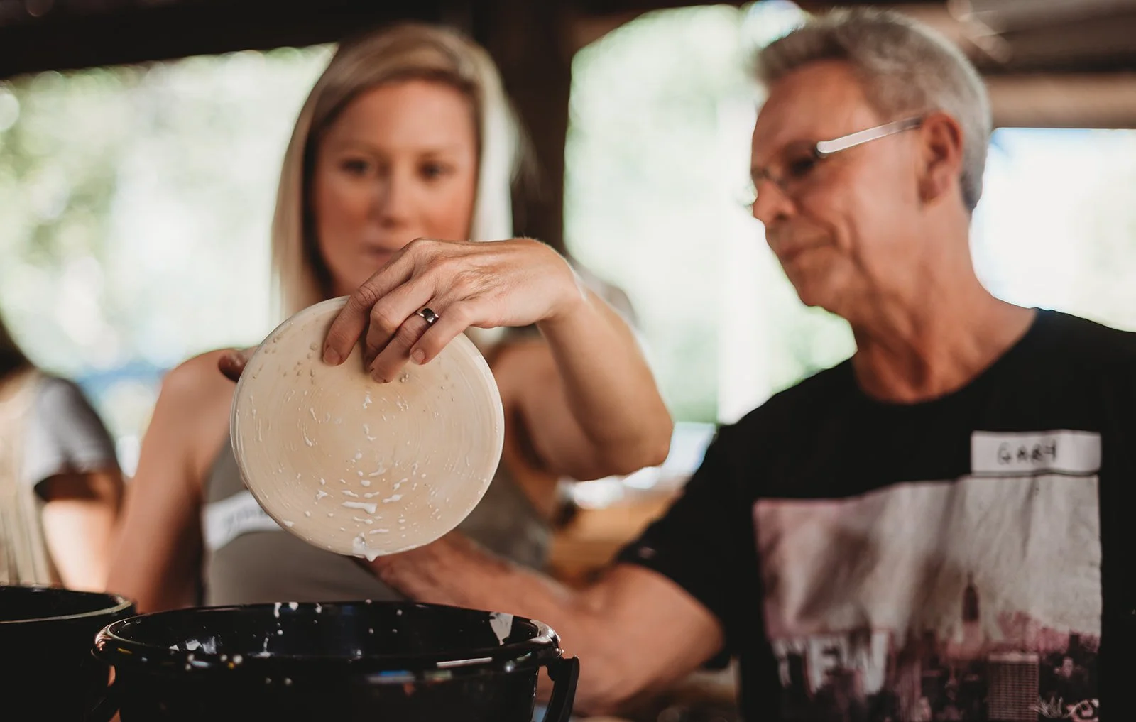 A woman pouring cheese into a pot held by a man at a gathering or party.