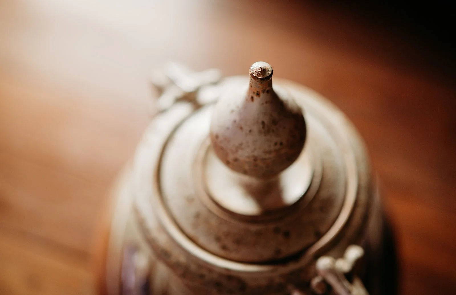 Close-up of a decorative vintage teapot lid with a rounded handle on top, featuring a speckled, weathered surface, resting on a wooden surface.