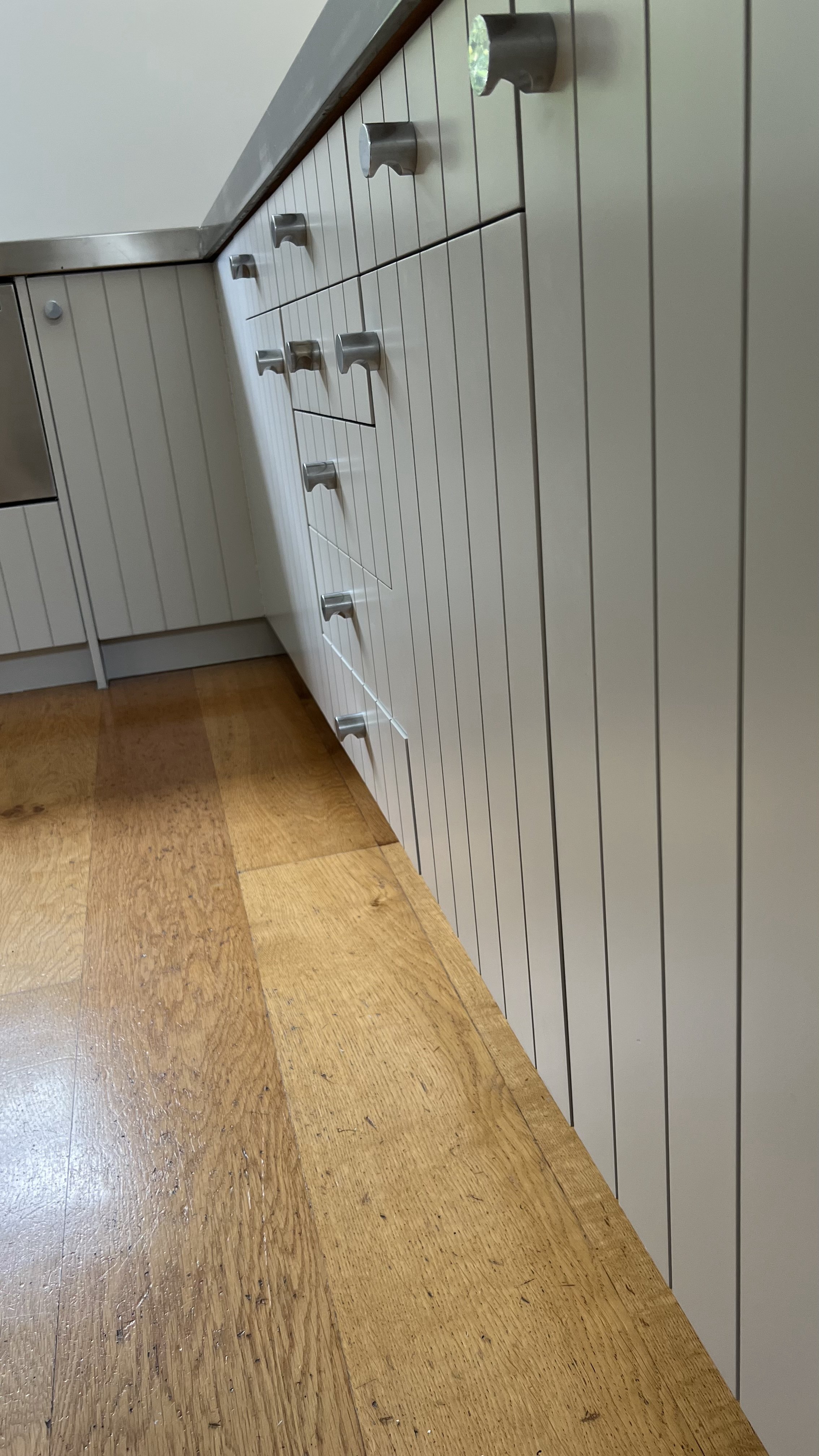 Close-up of a row of white cabinets with silver knobs, situated in a room with wooden floorboards.