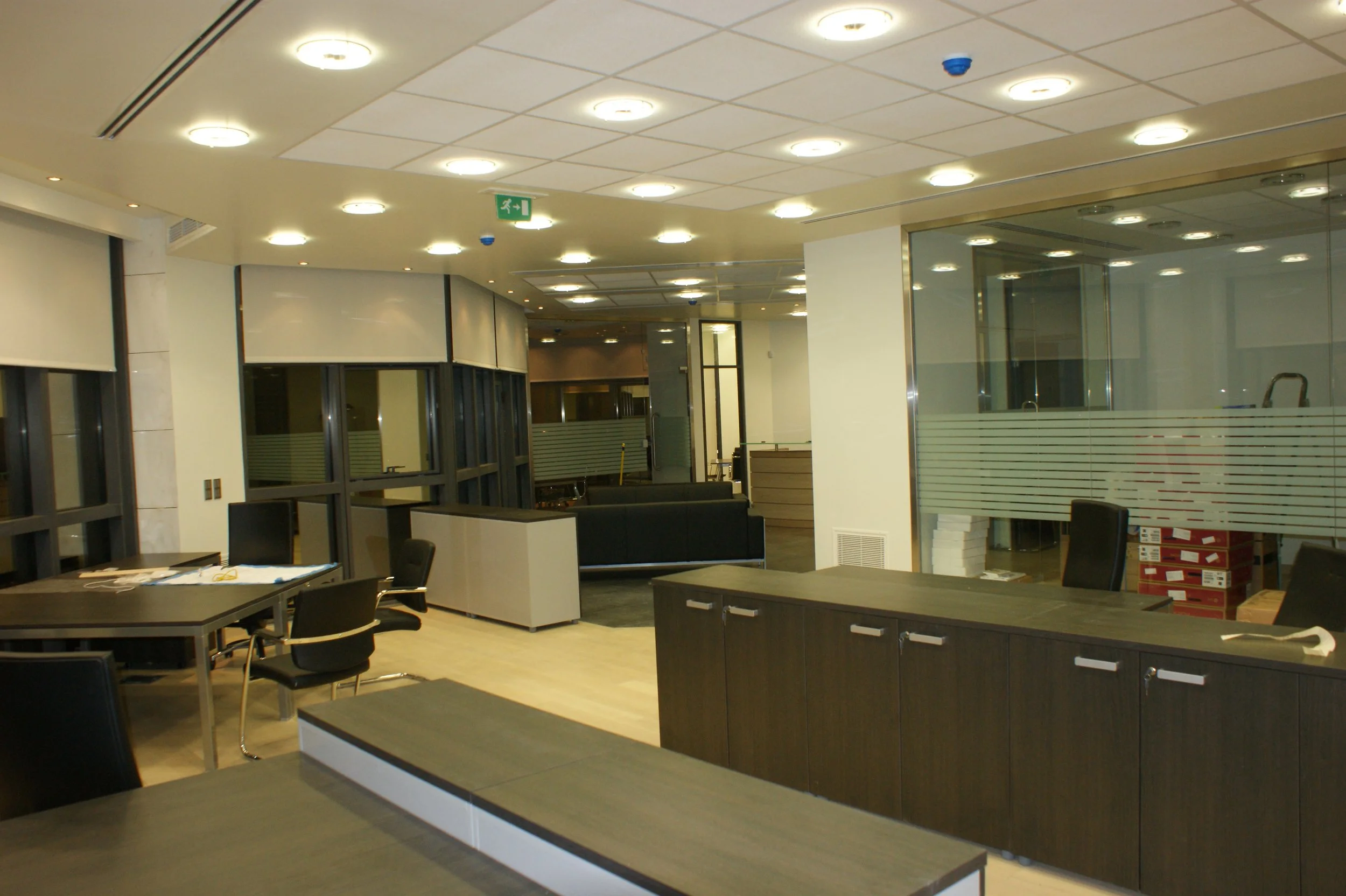 Interior of an office or reception area with tables, chairs, glass dividers, and ceiling lights.