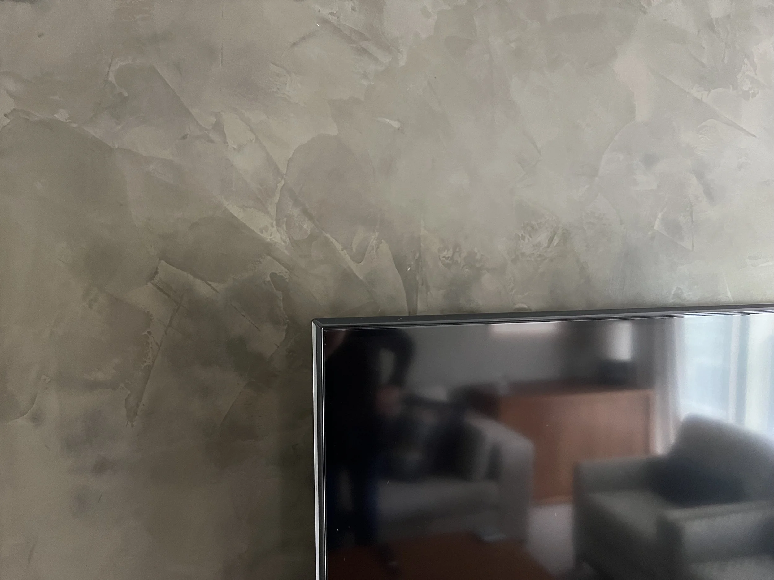 Close-up of a wall with a textured, stone-like finish and the edge of a metal appliance or fixture at the bottom right corner.