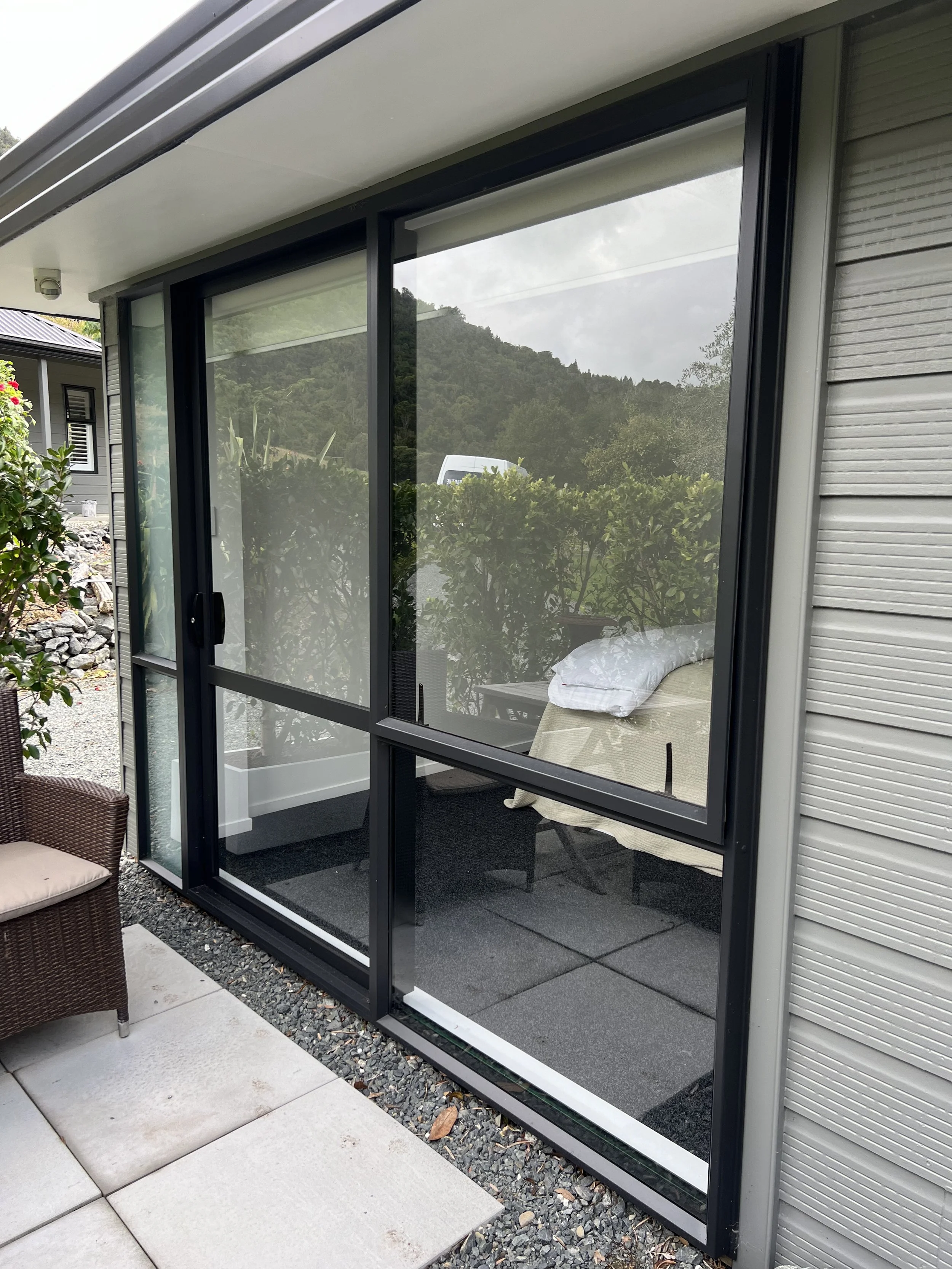 A house with a screened-in porch area with sliding glass doors, outdoor furniture, and a view of lush green trees and hills in the background.