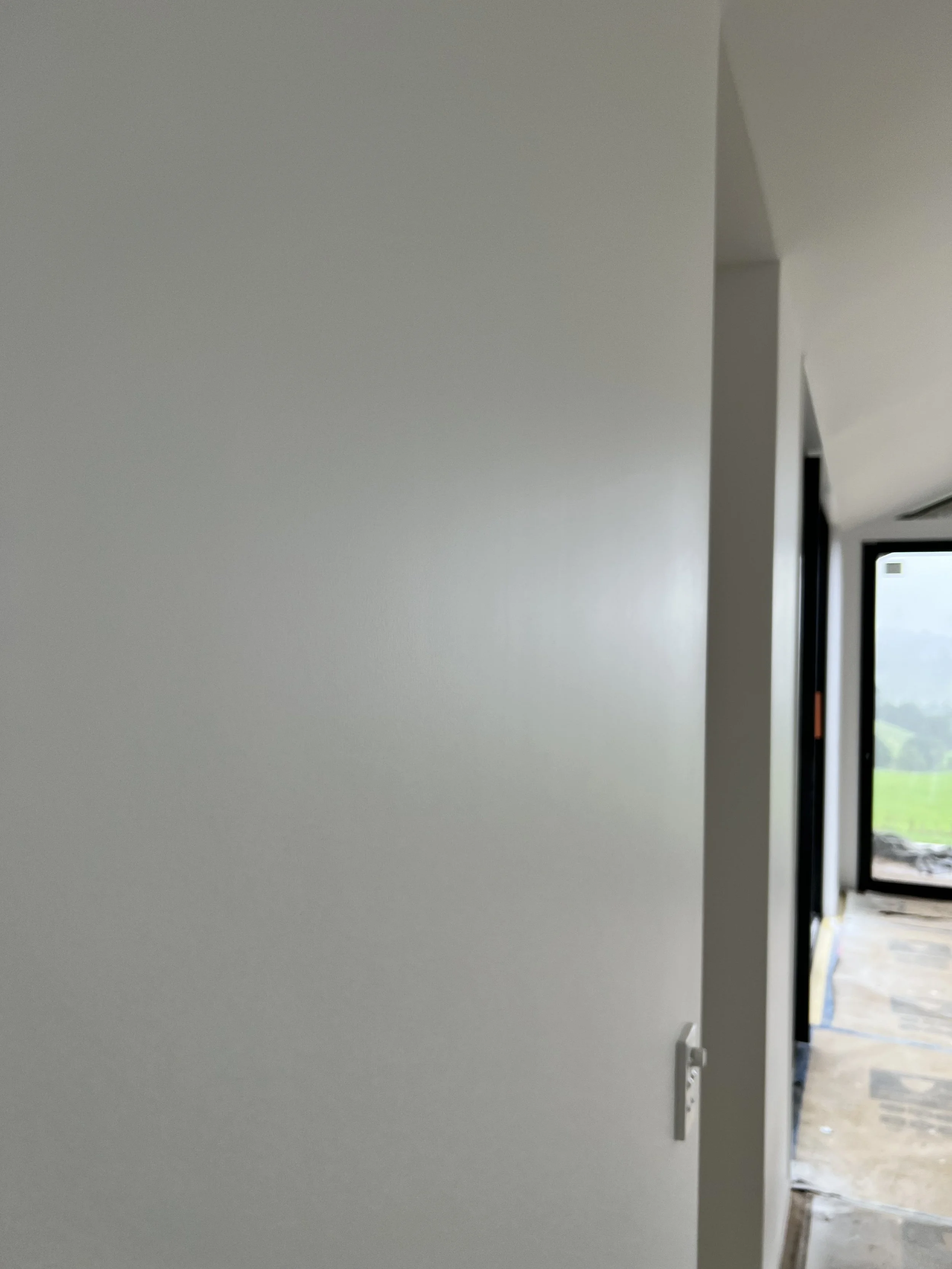 An interior view of a new building under construction, showing partially hung white closet doors and a doorway leading to an unfinished room with construction materials and a window with a scenic view outside.