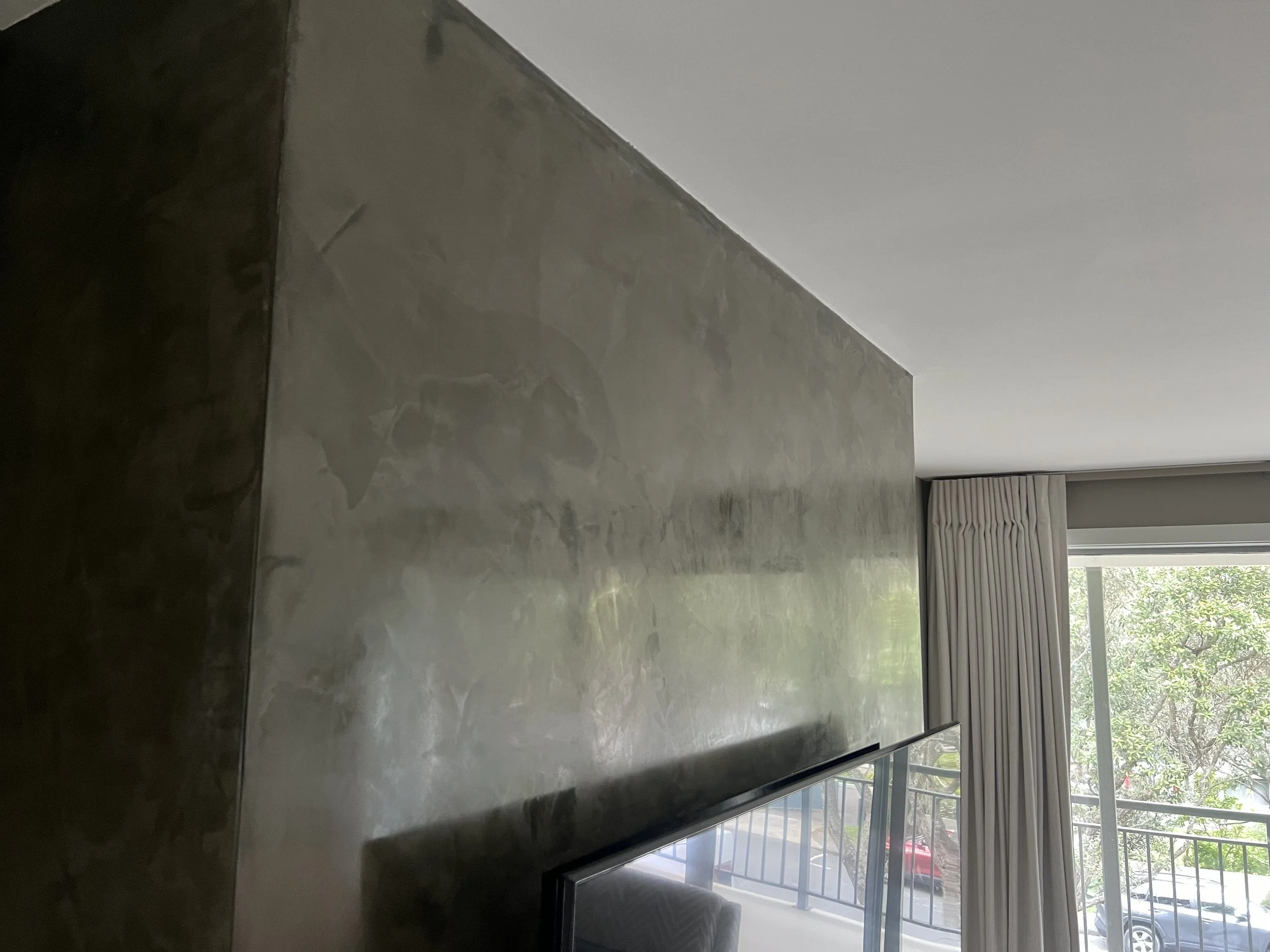 Interior photo of a venetian stucco finish on fireplace  with a window and curtains in the background.