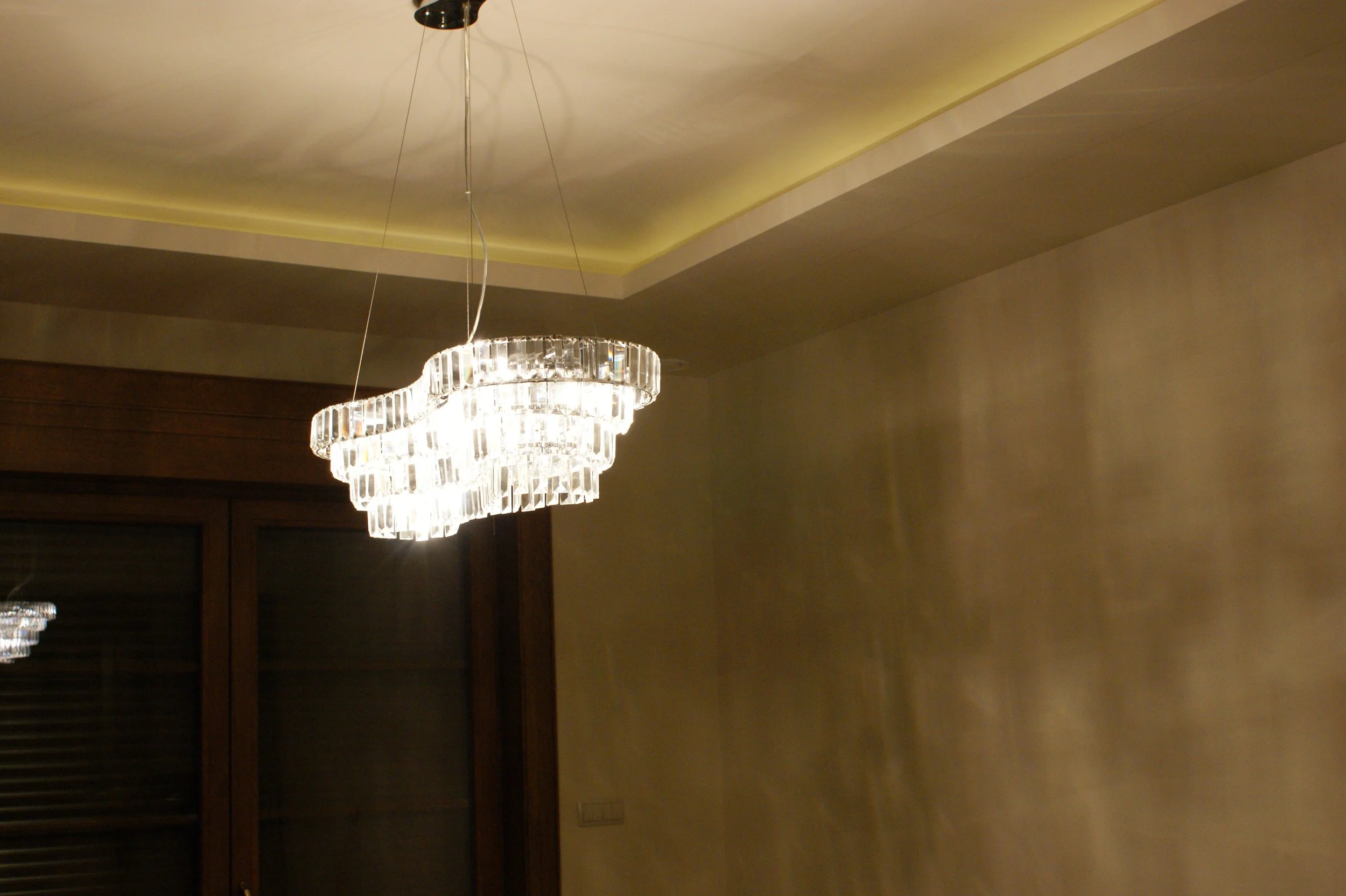 A luxurious chandelier hanging from the ceiling of an elegant room with warm lighting and beige-colored walls.