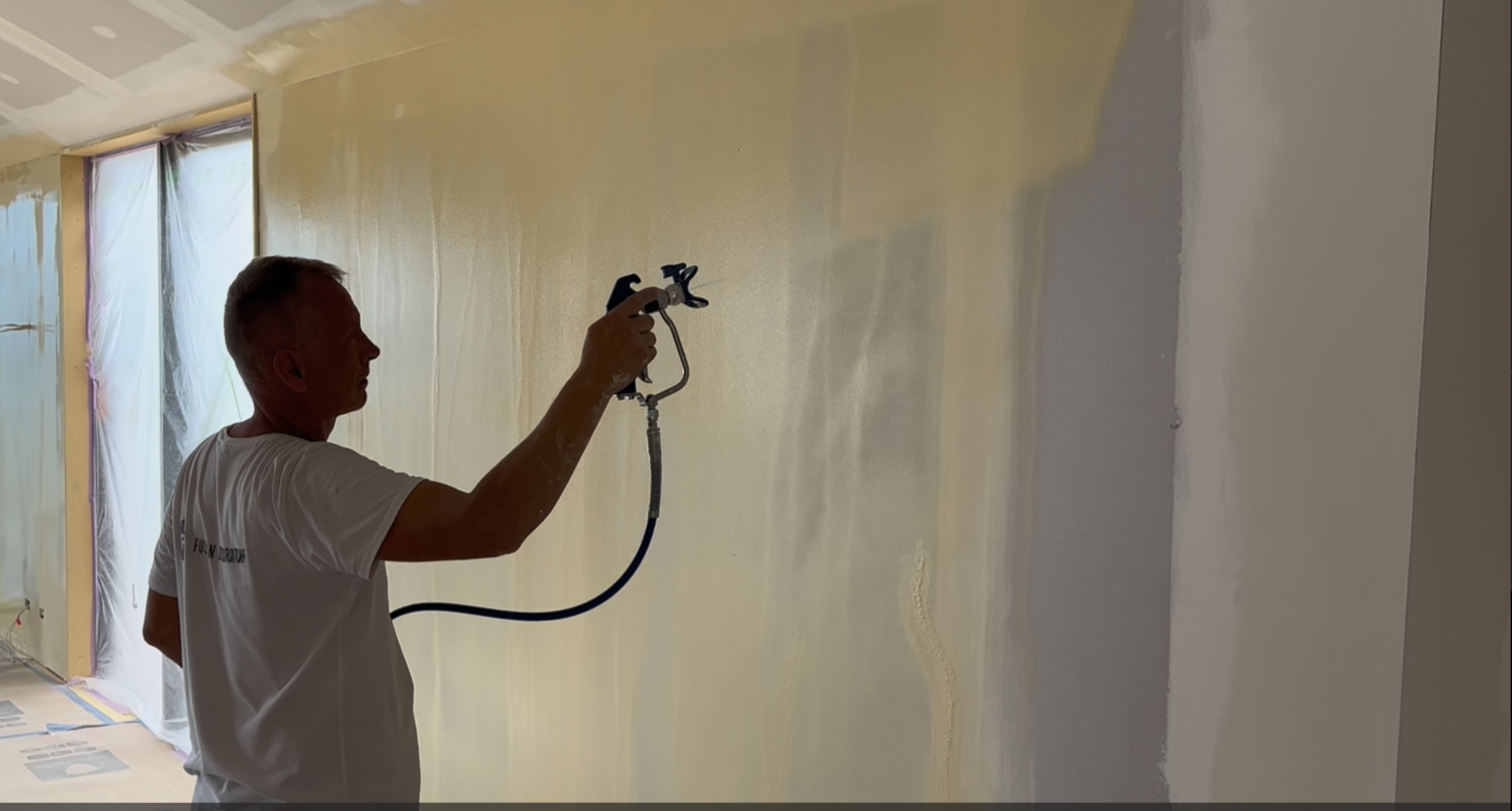 A man using a sprayer to paint a wall in a room under renovation.