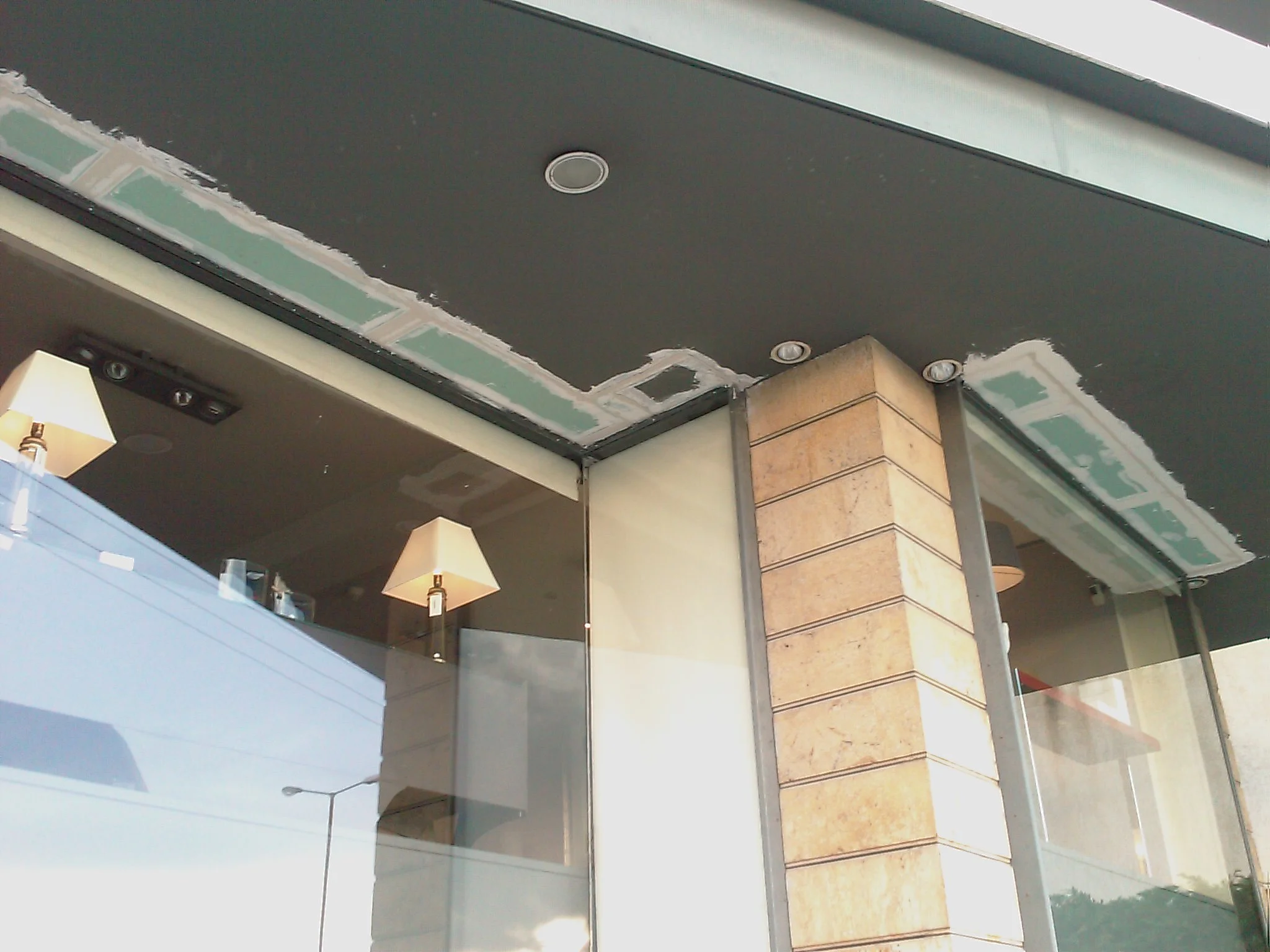 Interior of a building under renovation with partially installed drywall, recessed lighting, a column with tiling, and lamps hanging from the ceiling.