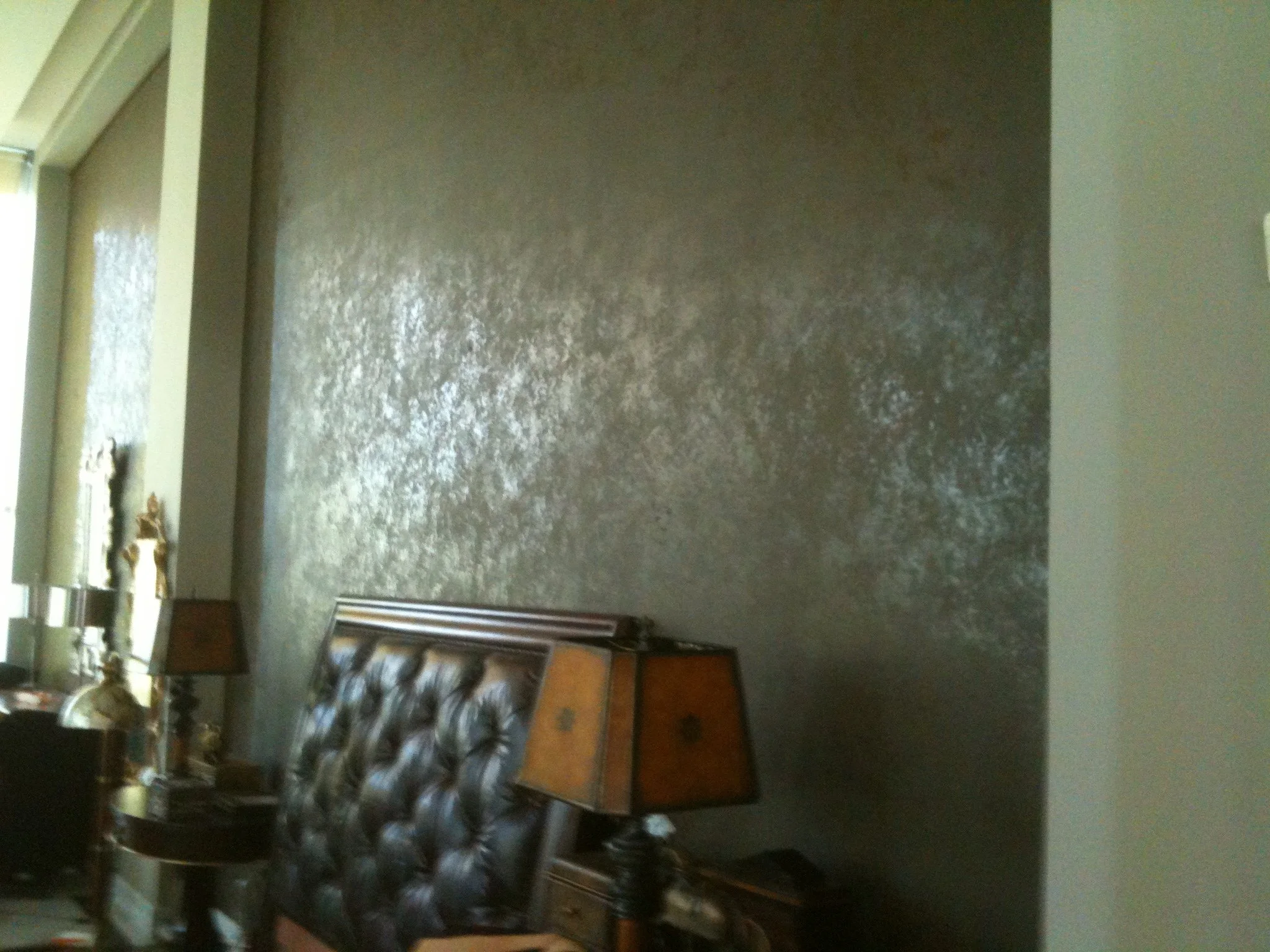 A dark green wall with a small section of a window frame and a wooden counter with a few decorative items. Part of a wooden chair with a patterned cushion is visible in the foreground.