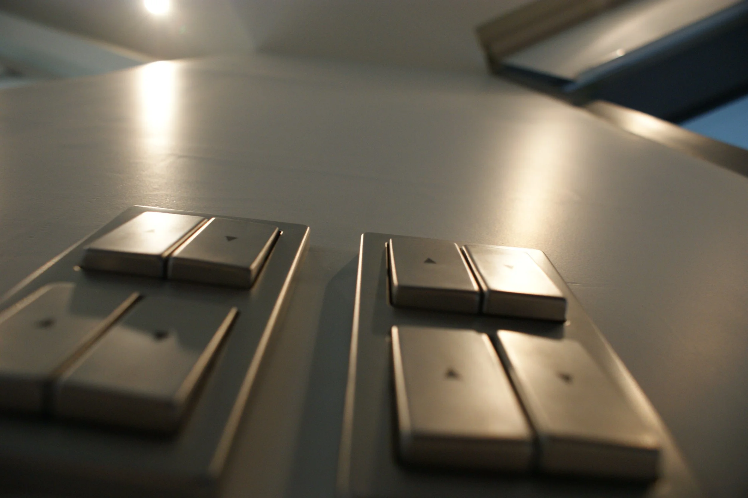 Close-up of a laptop keyboard and touchpad with a screen open in the background, lit by natural lighting.