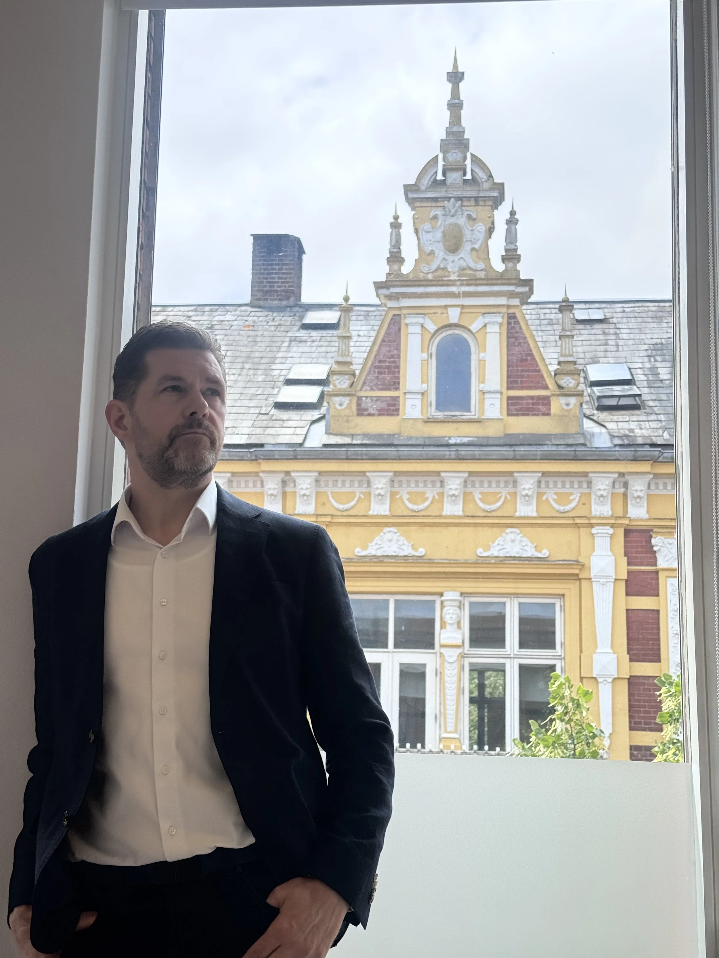 Bjarki Ágústsson standing beside a window overlooking historic architecture.