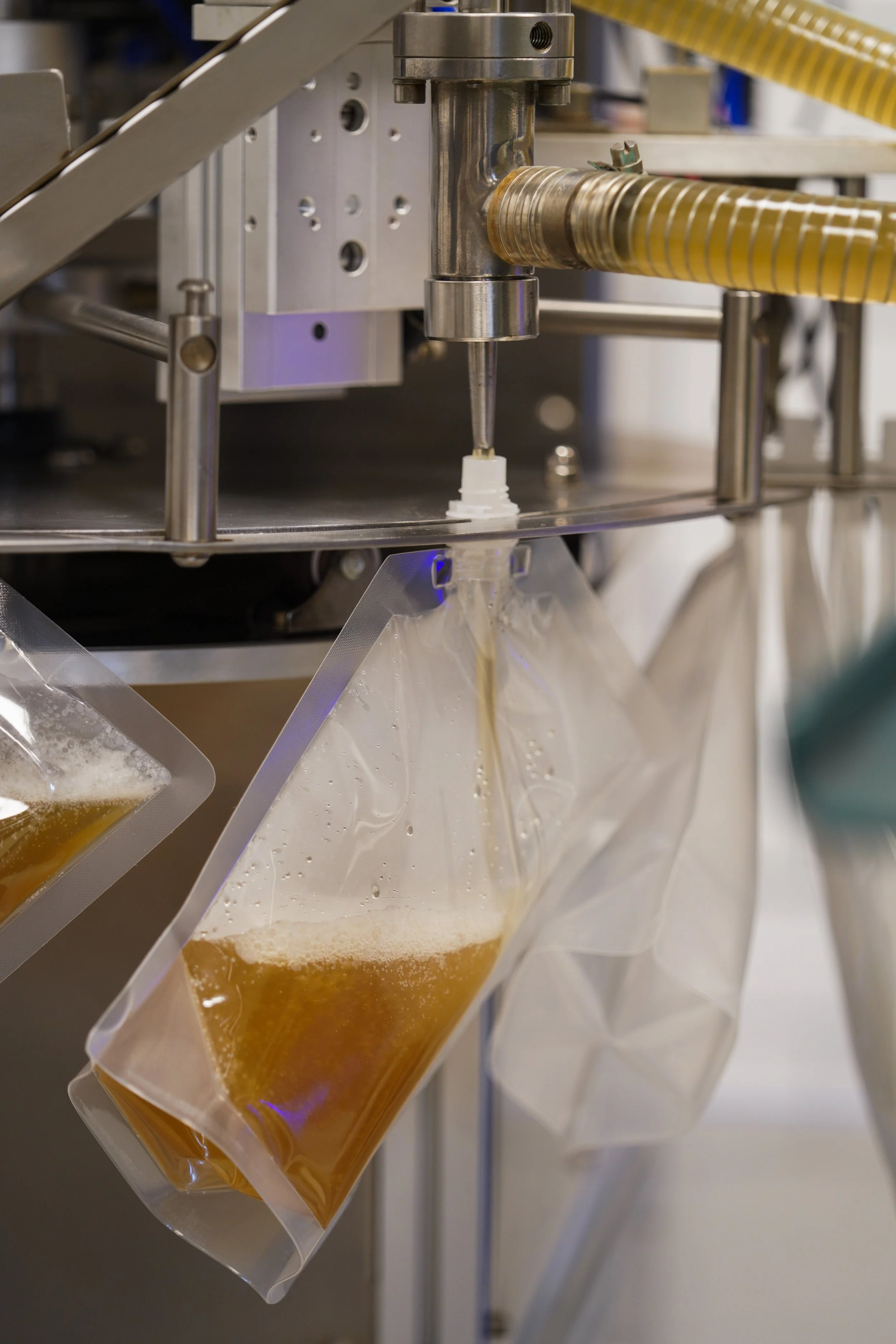 Industrial equipment dispensing liquid into transparent plastic bags, with hoses and metal components.