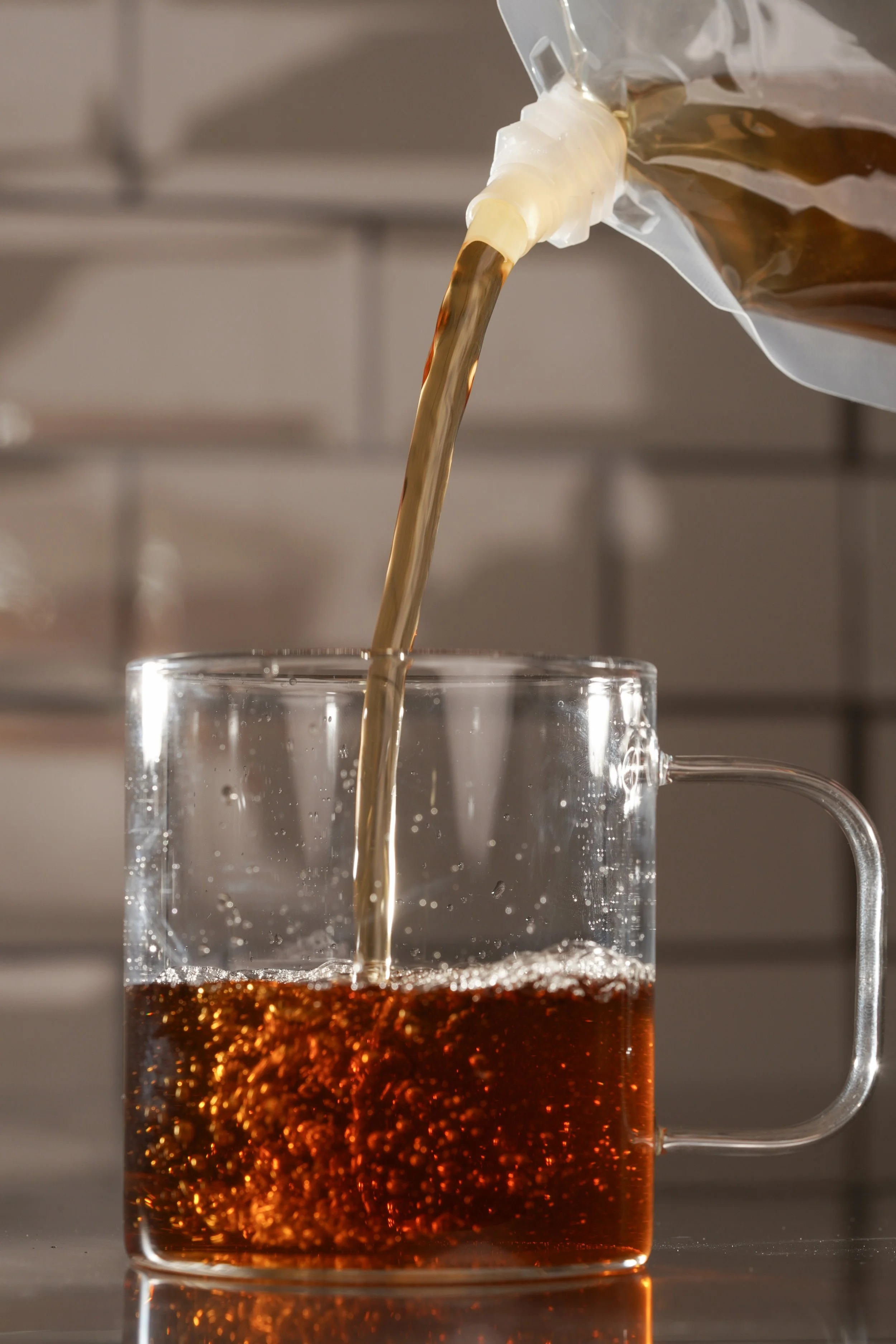 Coffee being poured from a plastic pouch into a clear glass mug.