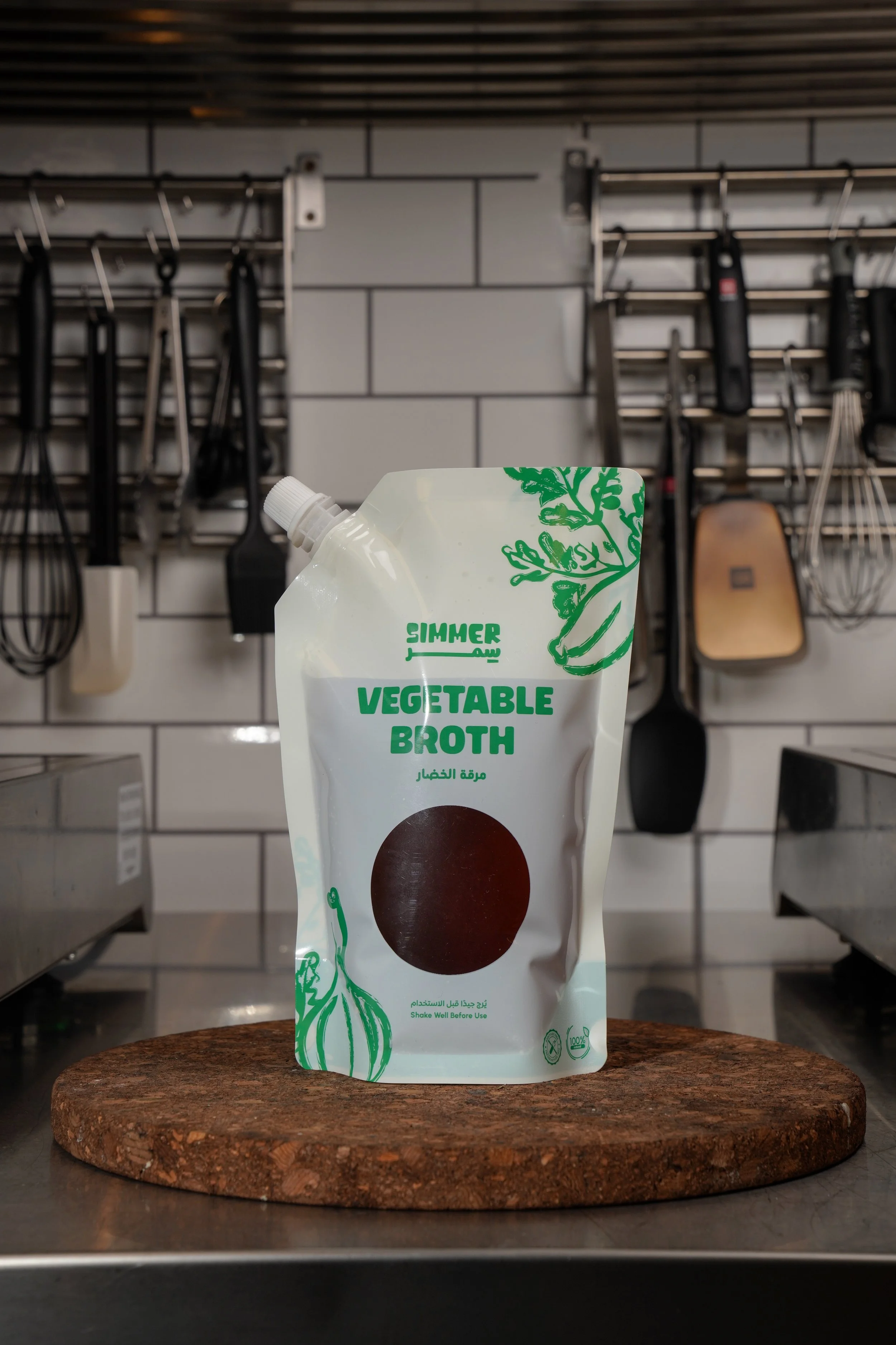A pouch of vegetable broth on a wooden surface with a kitchen wall and utensils in the background.