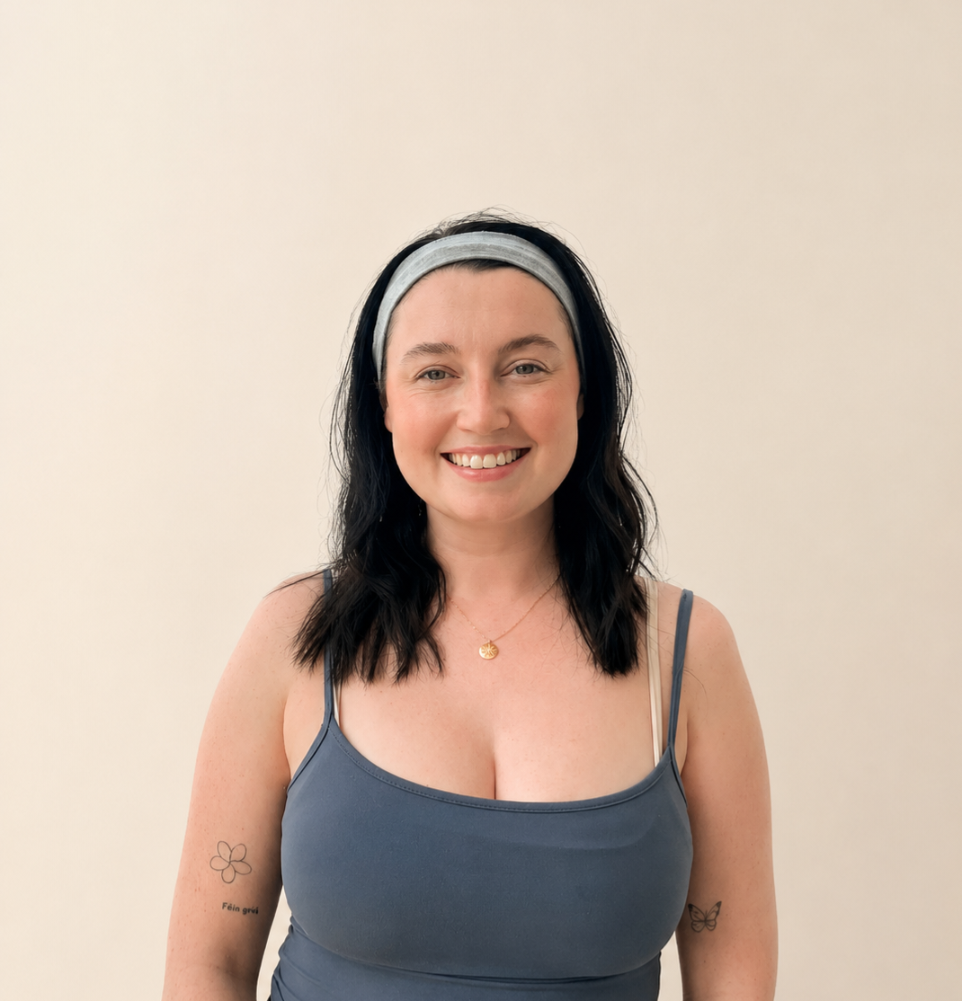 A woman with black wavy hair, wearing a gray headband and a blue tank top, smiling against a plain beige background.