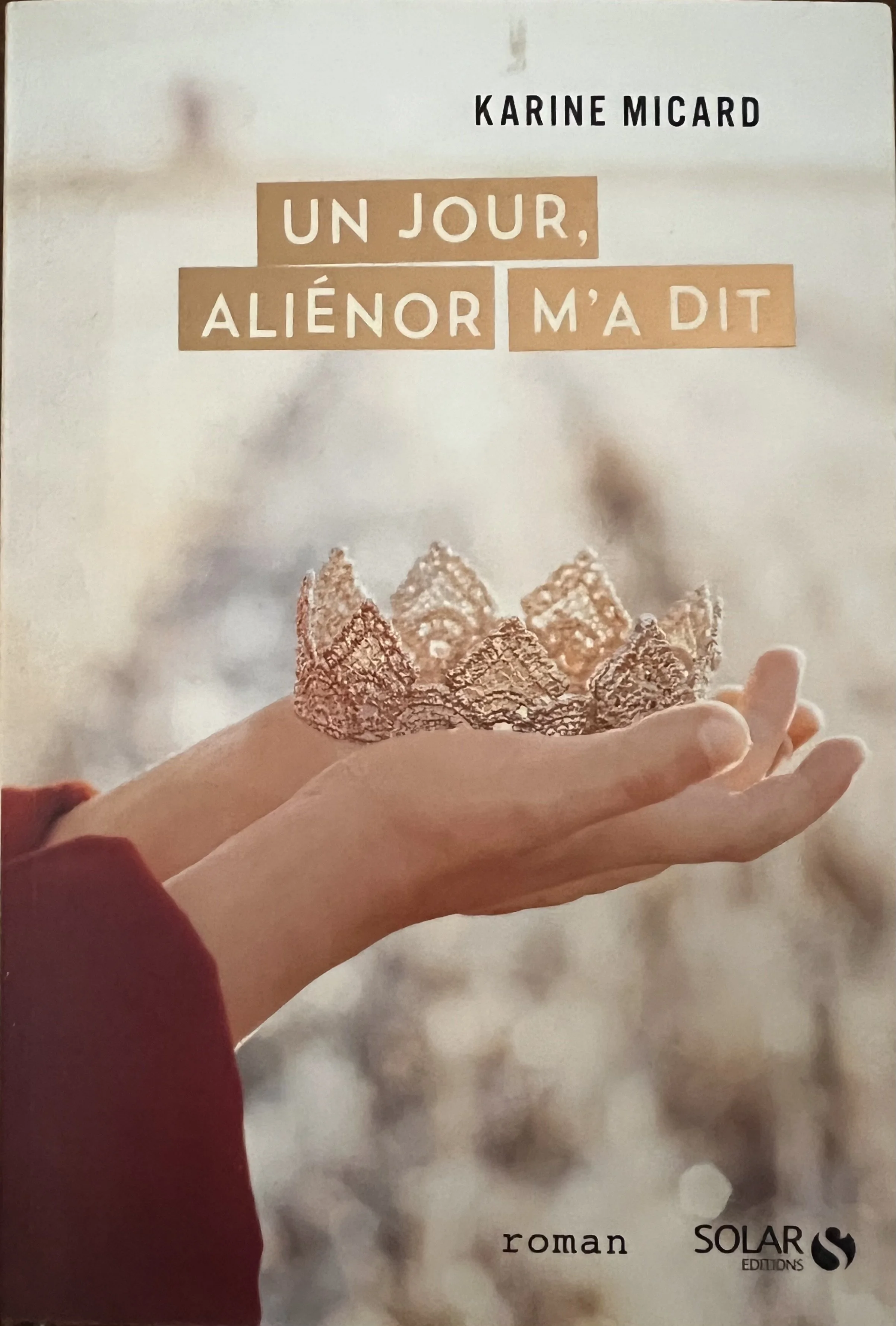 Couverture d'un livre intitulé "Un jour, alienor m'a dit" écrit par Karine Micard, montrant une main tenant une tiare faite de sel ou un motif en forme de couronne, avec un fond flou.